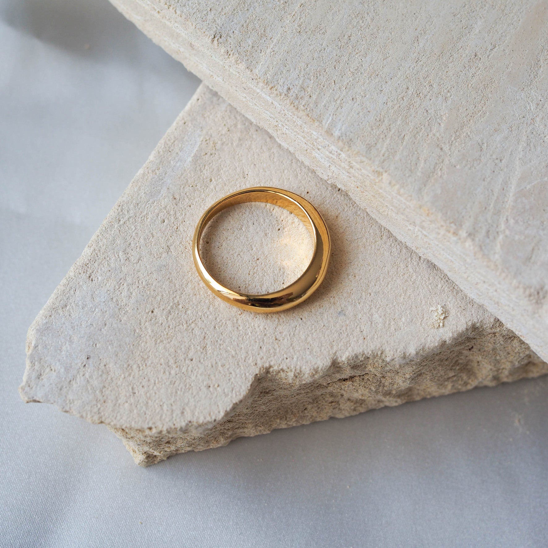 Close-up of a polished gold ring displayed on beige stone.