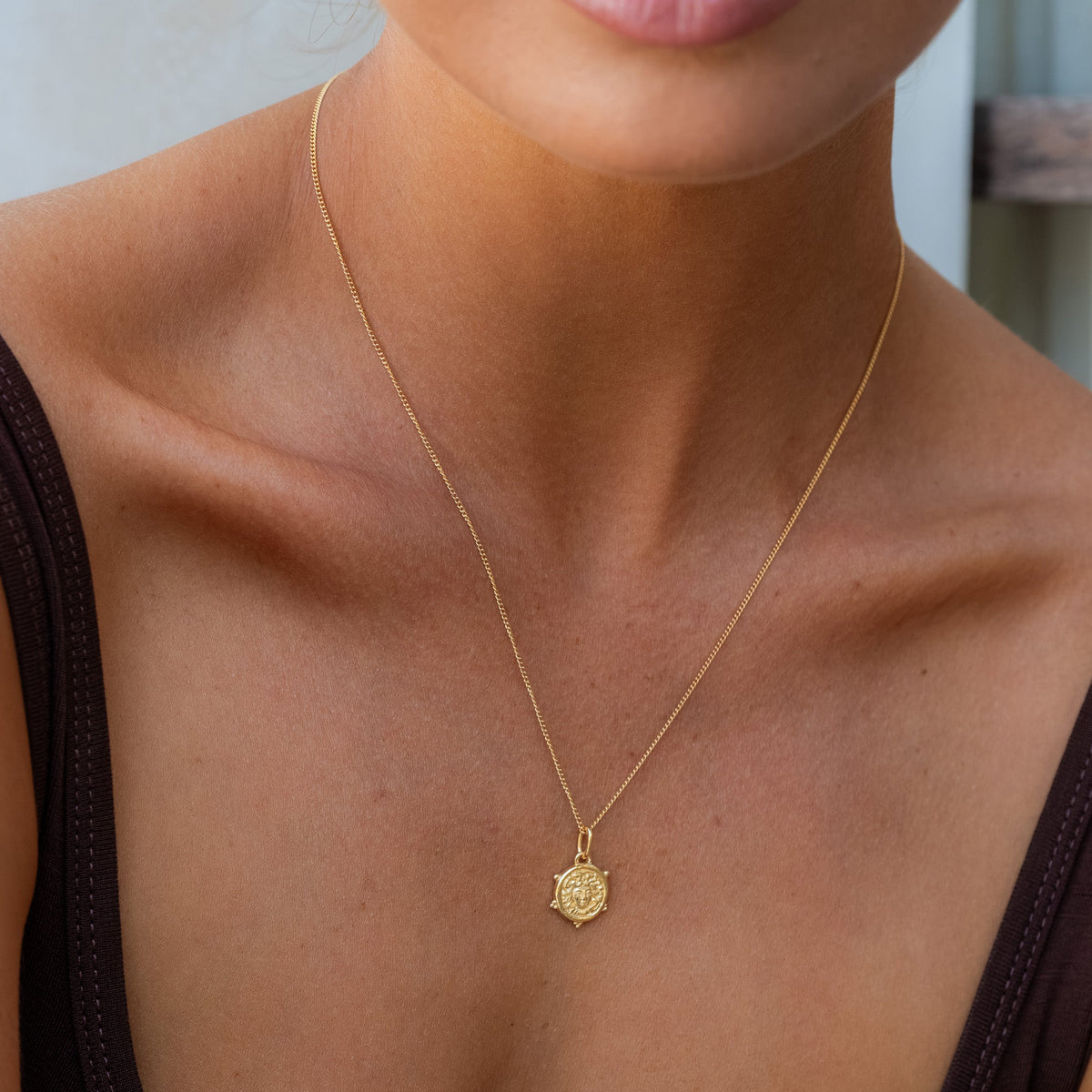 Woman wearing a delicate mini Medusa necklace gold
