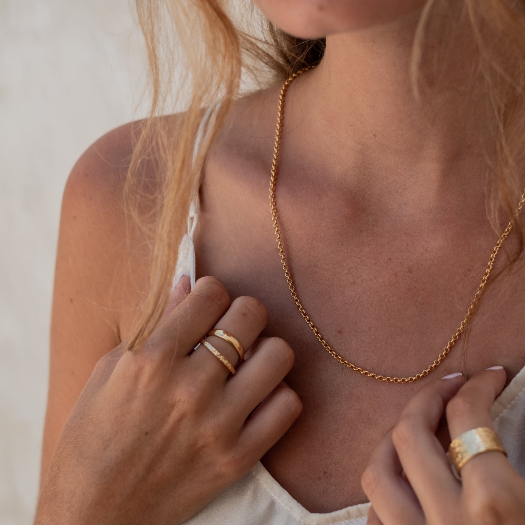 Close-up of a woman's neck and shoulders wearing a gold chain necklace .