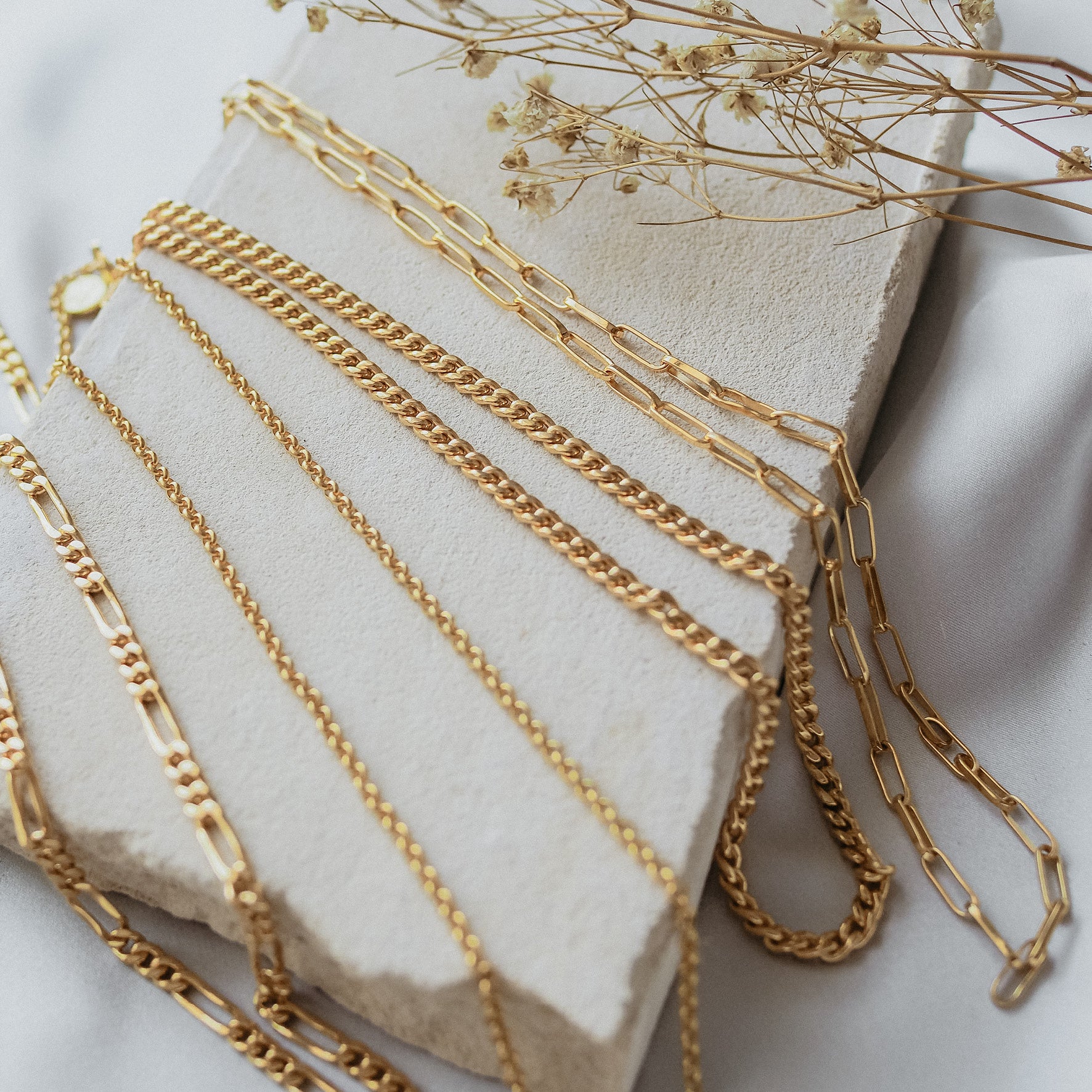 a multiple necklaces gold displayed on beige stone and dried flowers