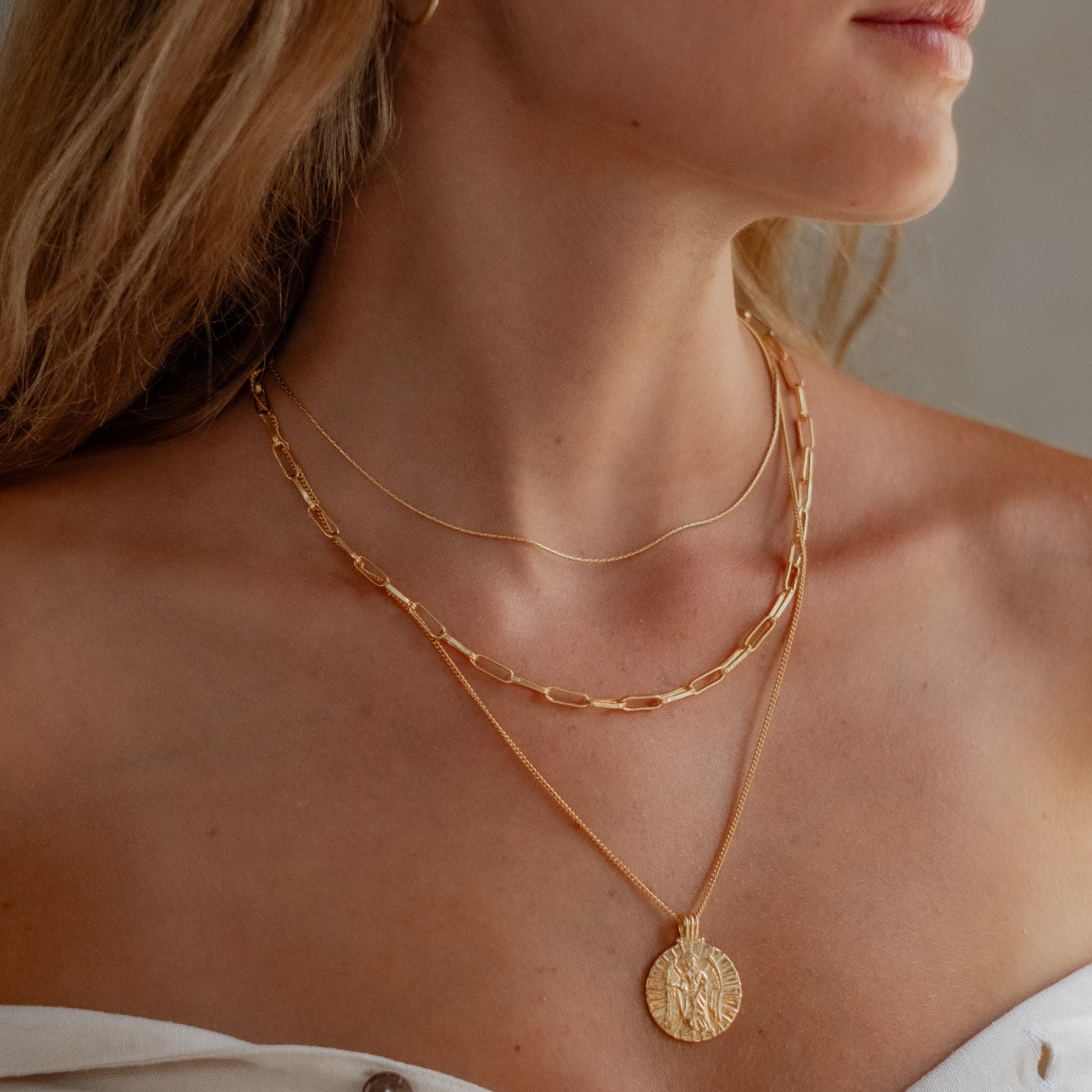 a woman with blonde hair wearing multiple necklaces gold