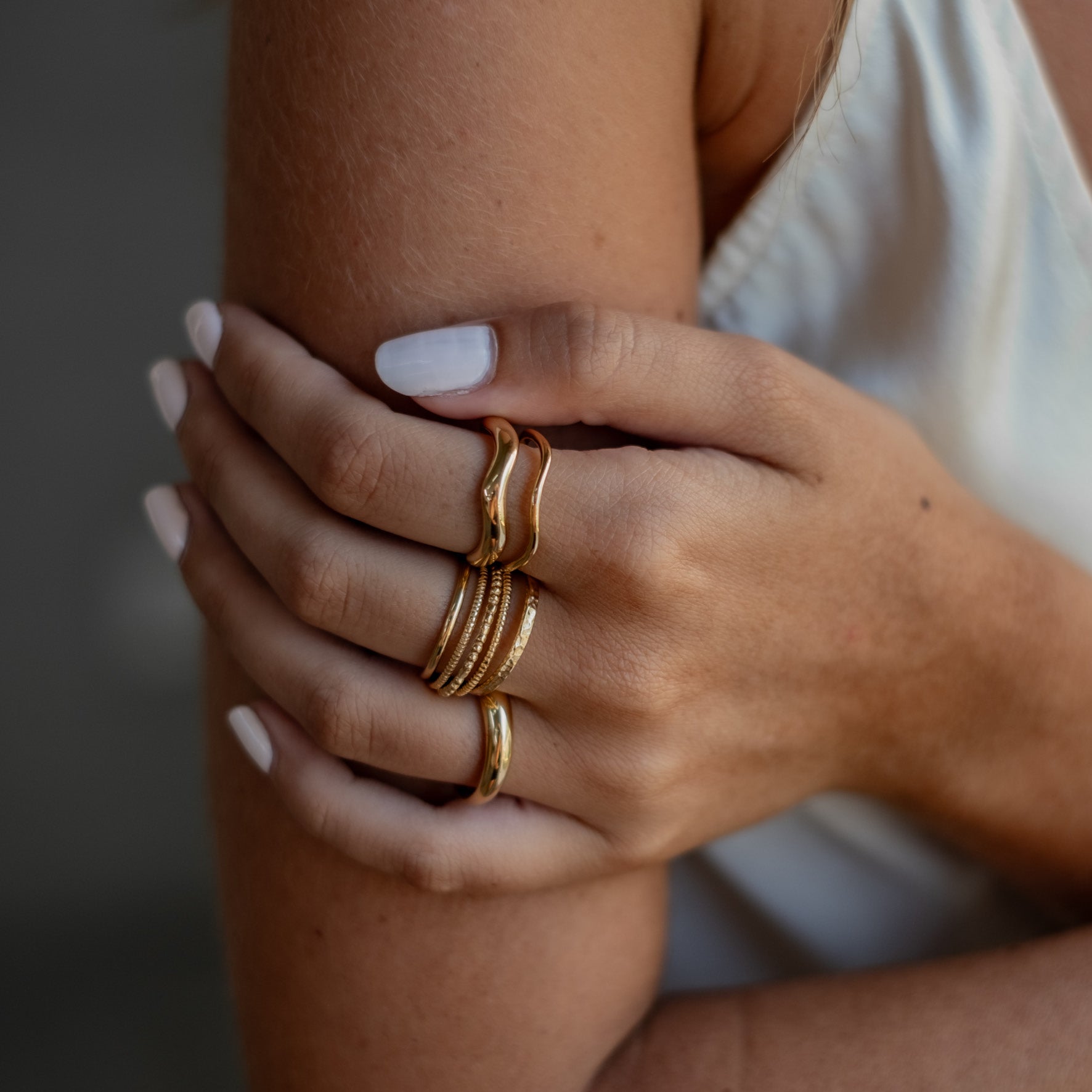 Close-up of a woman's arms crossed over her chest, showcasing multiple gold rings with various designs on her fingers.