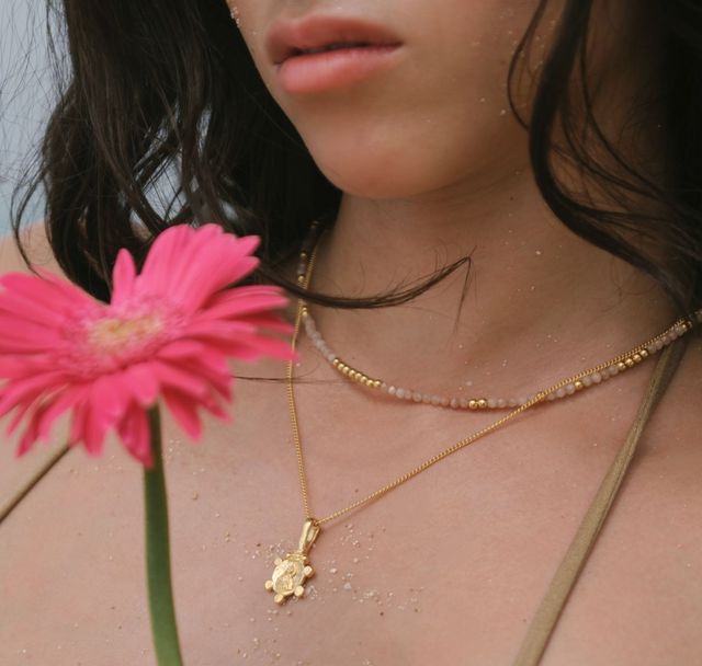 a woman with her layered necklace holding a pink flower