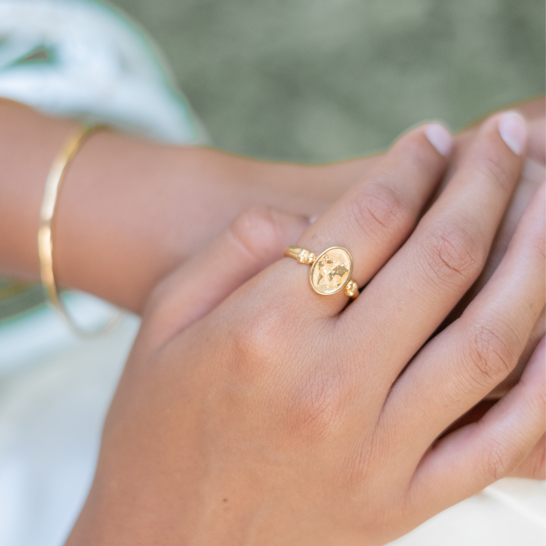 A close-up of a gold ring with a sun and waves design on a woman's finger, alongside a gold bracelet.