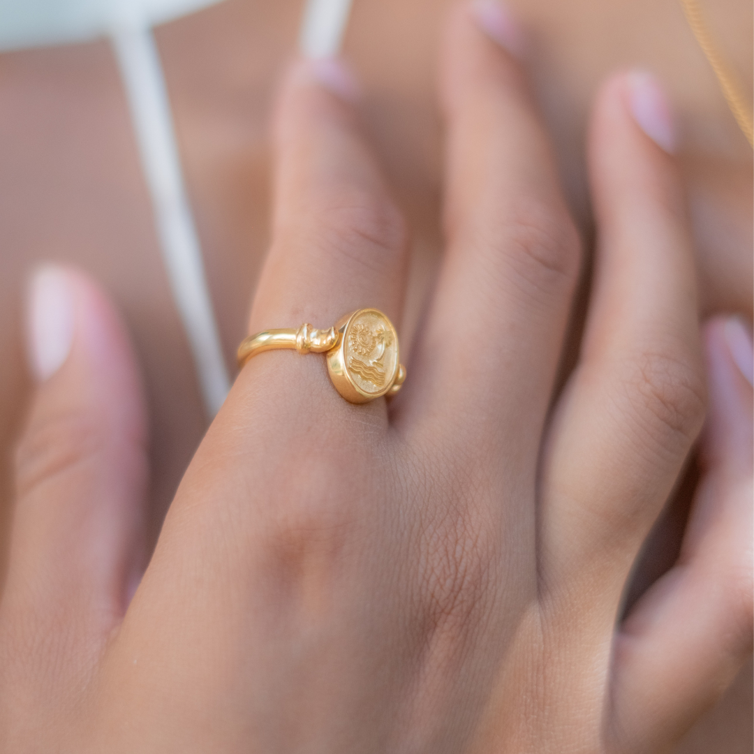 A close-up of a gold ring with an intricately designed saint figure on a woman's finger.