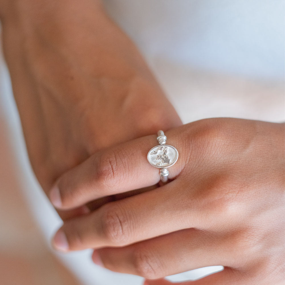 A close-up of a silver ring with a sun and waves design on a woman's finger.