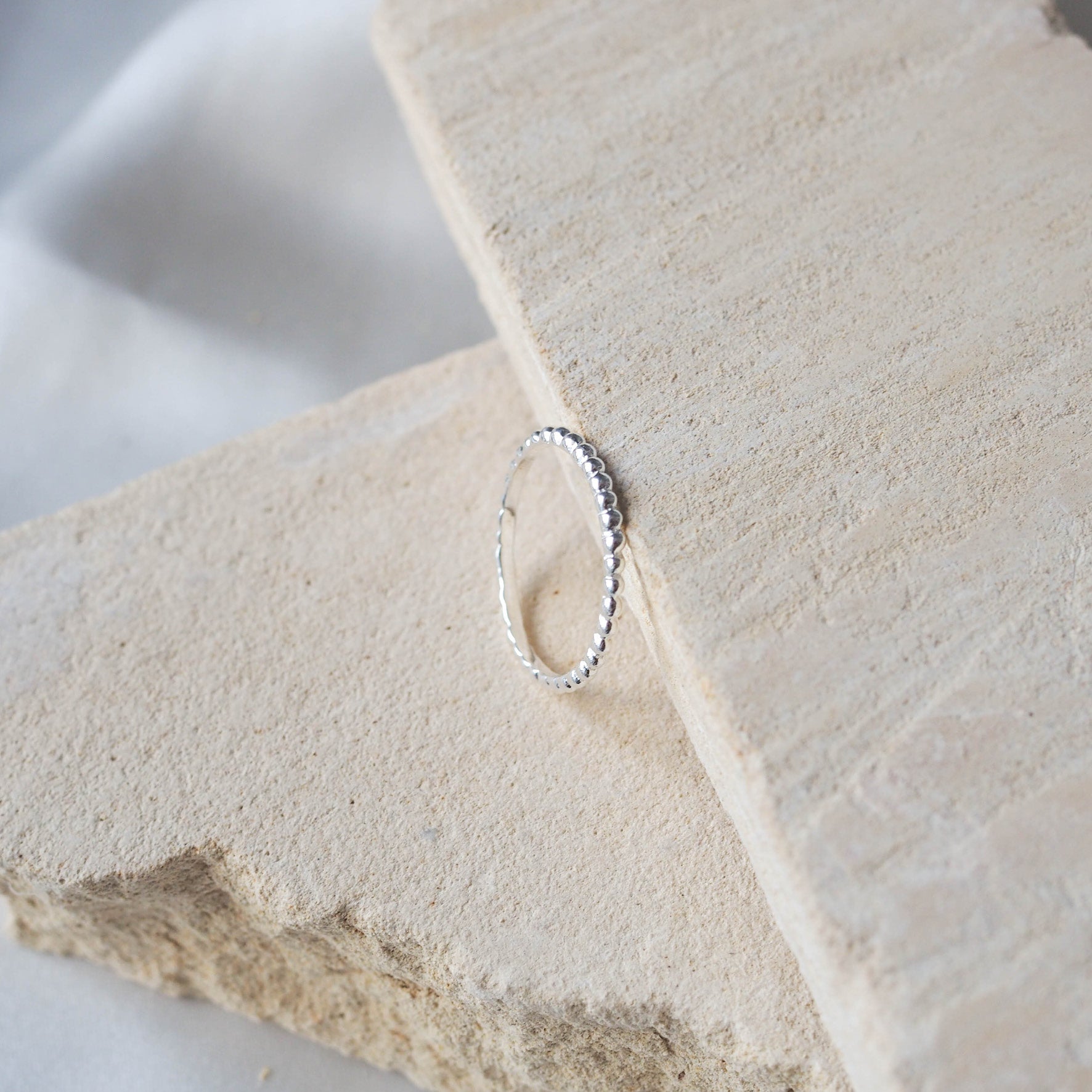 Top view of a silver beaded ring displayed on a textured beige stone.