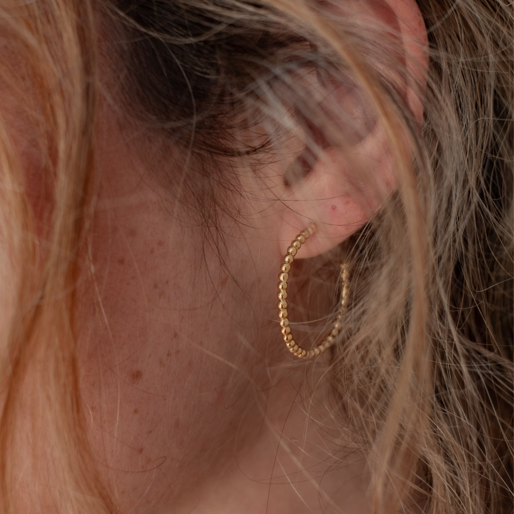 Close-up of a woman with brown hair wearing one gold earring