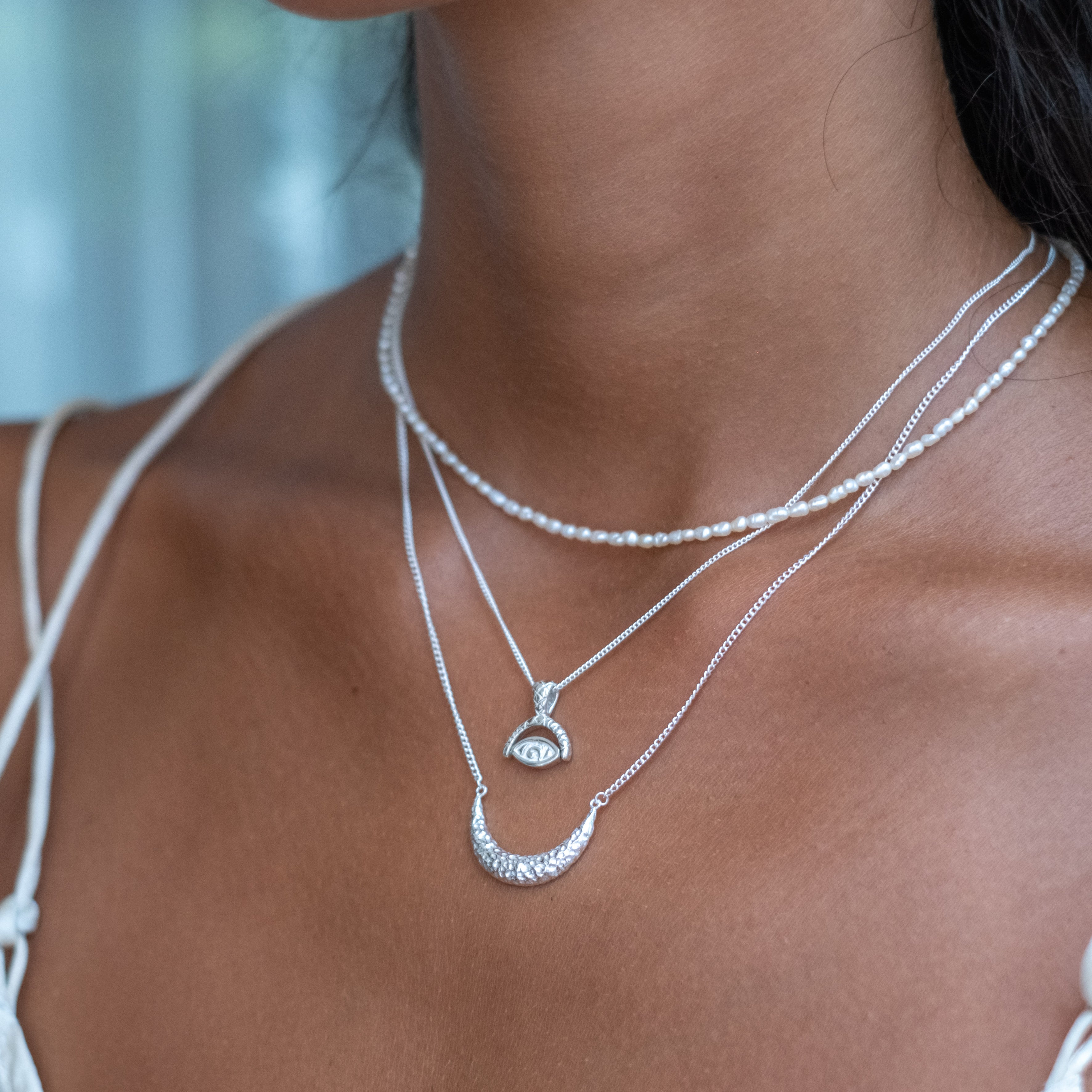 A person wearing a white tank top and two layered silver necklaces, one featuring a crescent moon pendant
