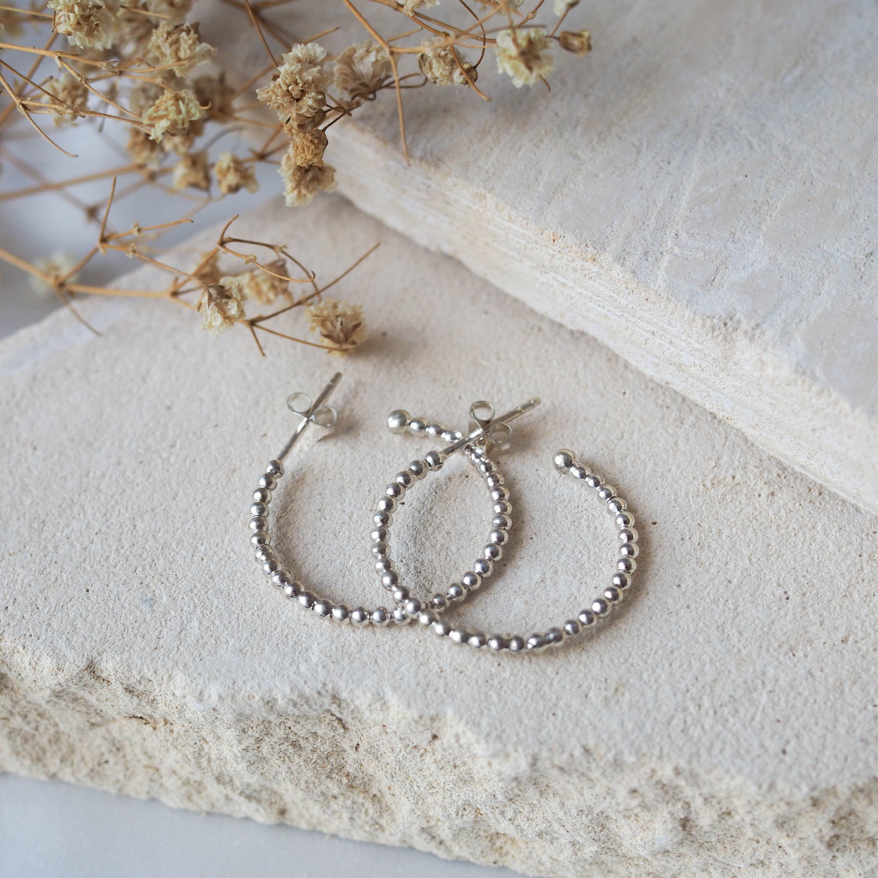 Pair of silver earring displayed on a textured beige stone