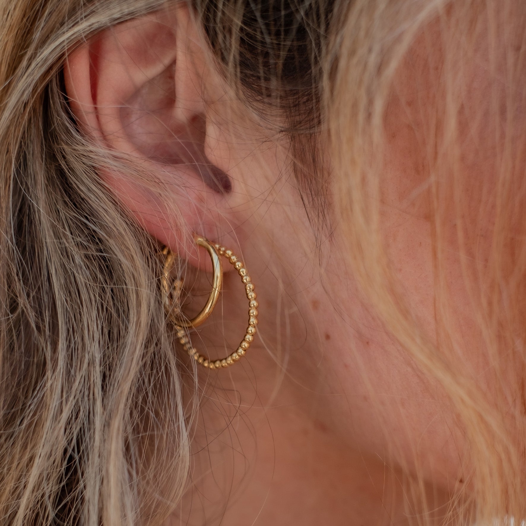 Close-up of a woman with brown hair wearing two gold earrings in different sizes, one smooth and one beaded