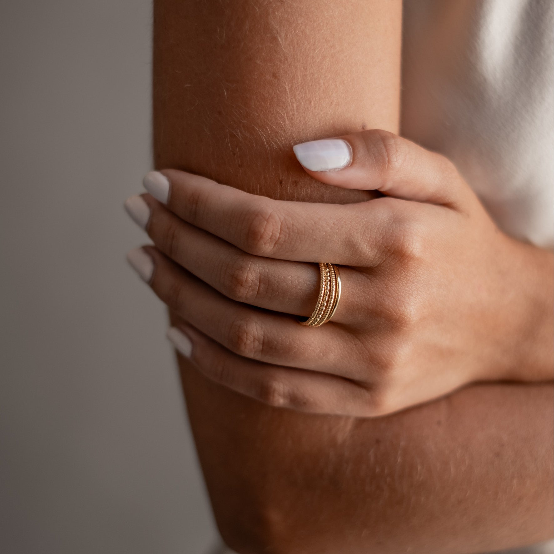 A person wearing a stack of gold rings on their finger, with their hand resting on their arm.
