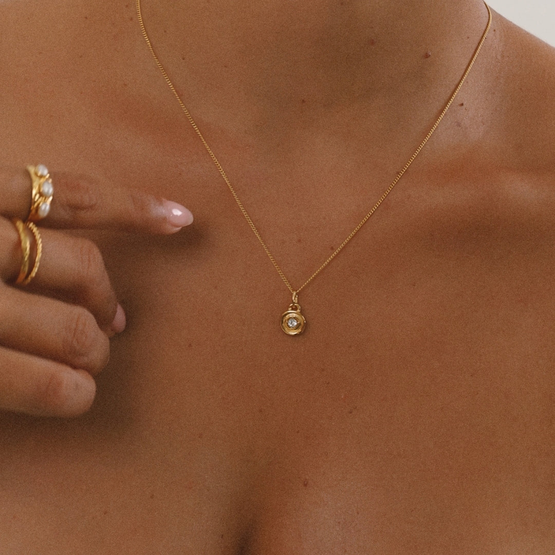 Gold necklace with a pendant on a person's neck, with a hand adjusting the necklace.