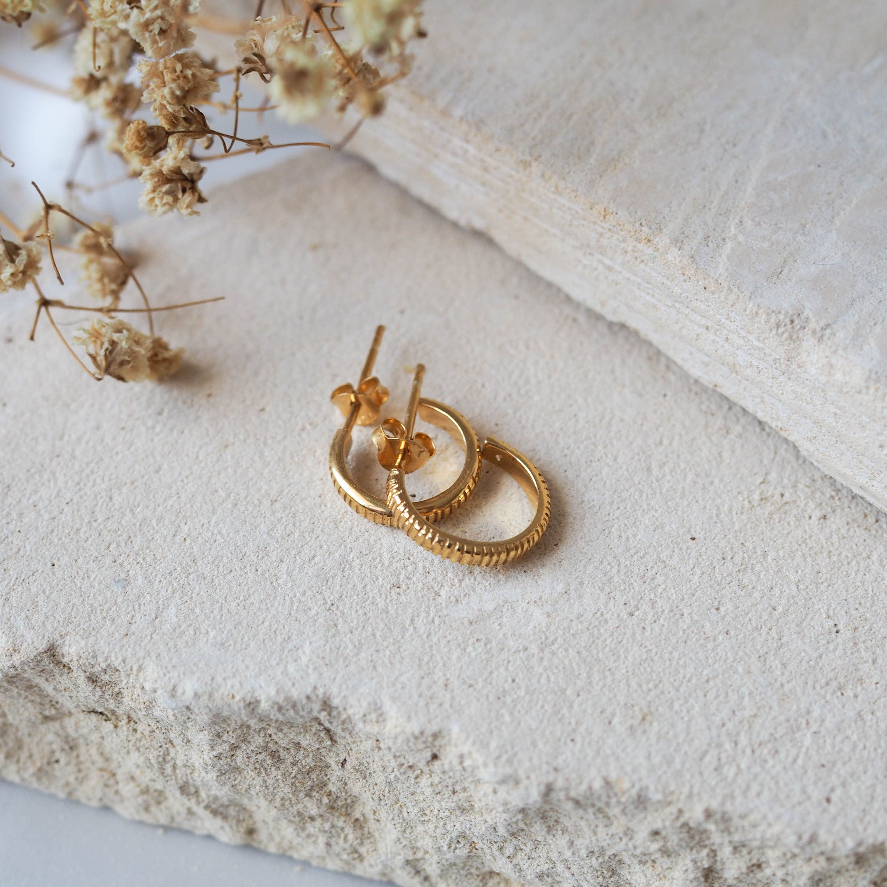 The MET Stripe Thin Earrings 12mm - Gold displayed on beige stone