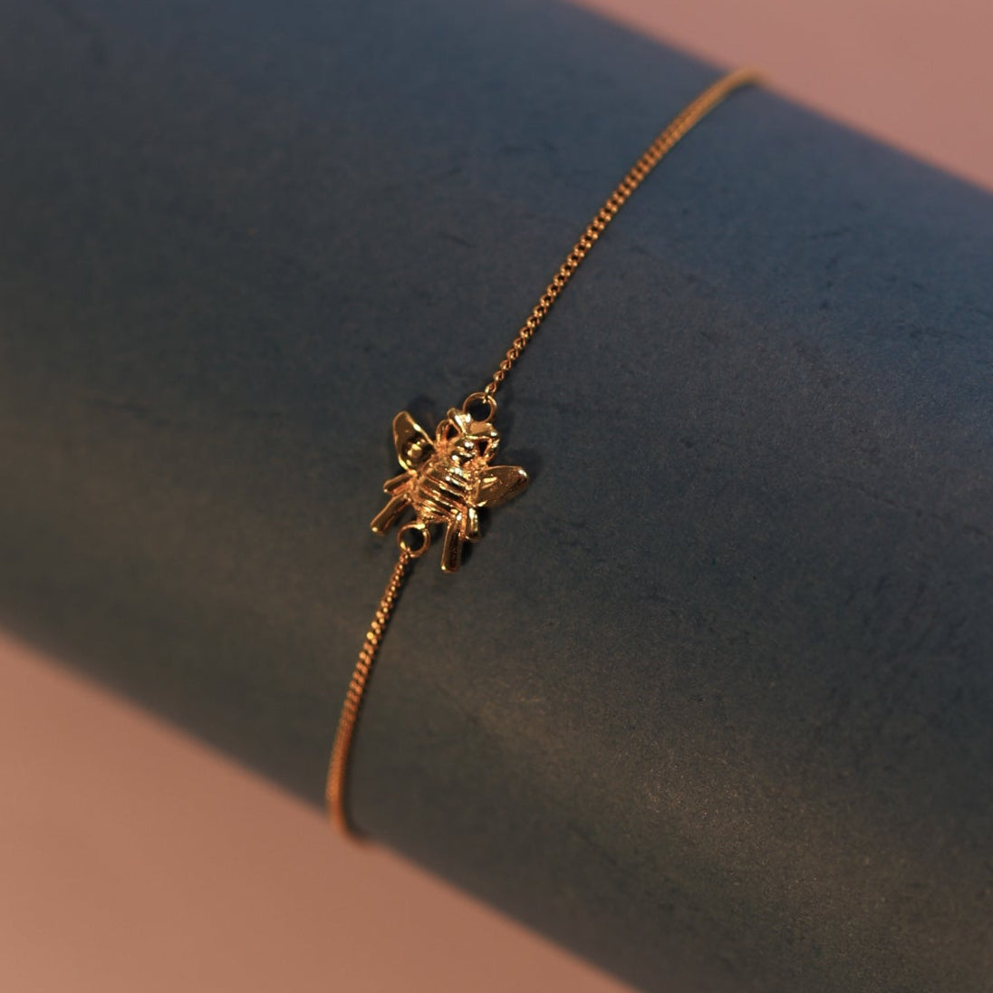 Gold bracelet on a dark blue surface with a soft pink background