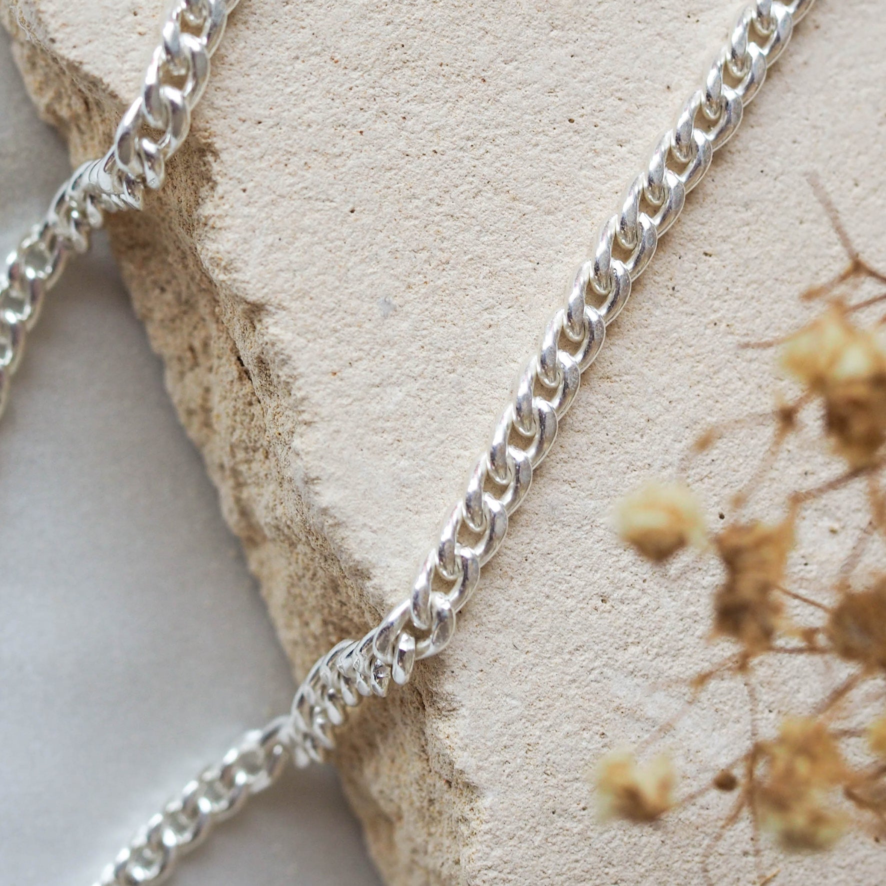 A silver chain bracelet with different link styles displayed on a textured beige stone