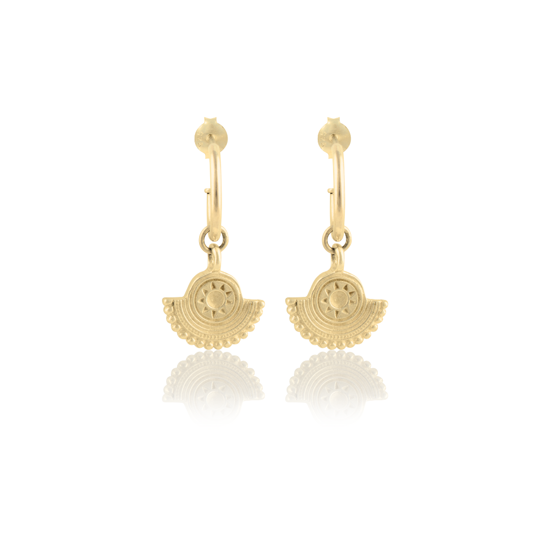 A pair of gold earrings with a circular sunburst design on a white background.