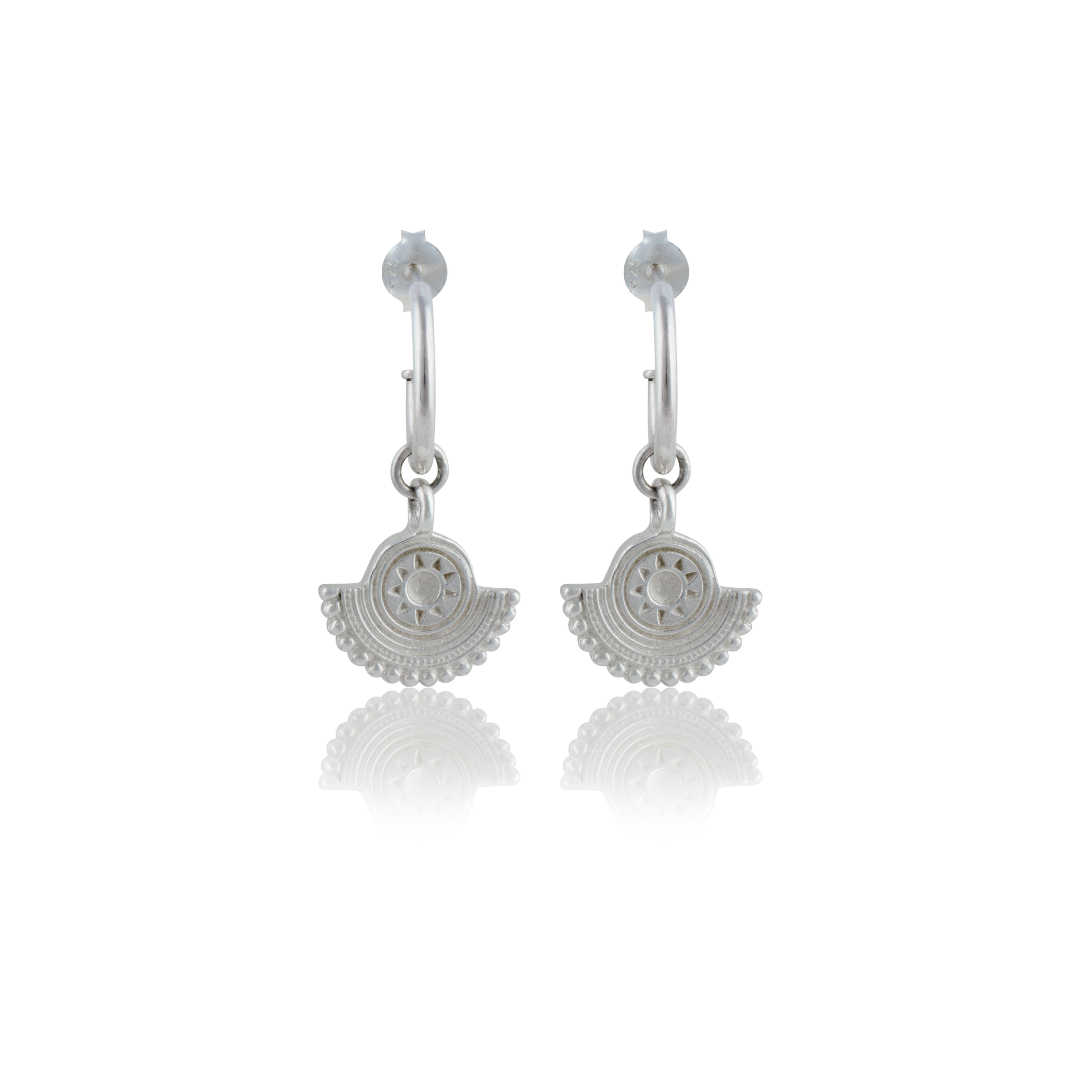A pair of silver earrings with a circular sunburst design on a white background.
