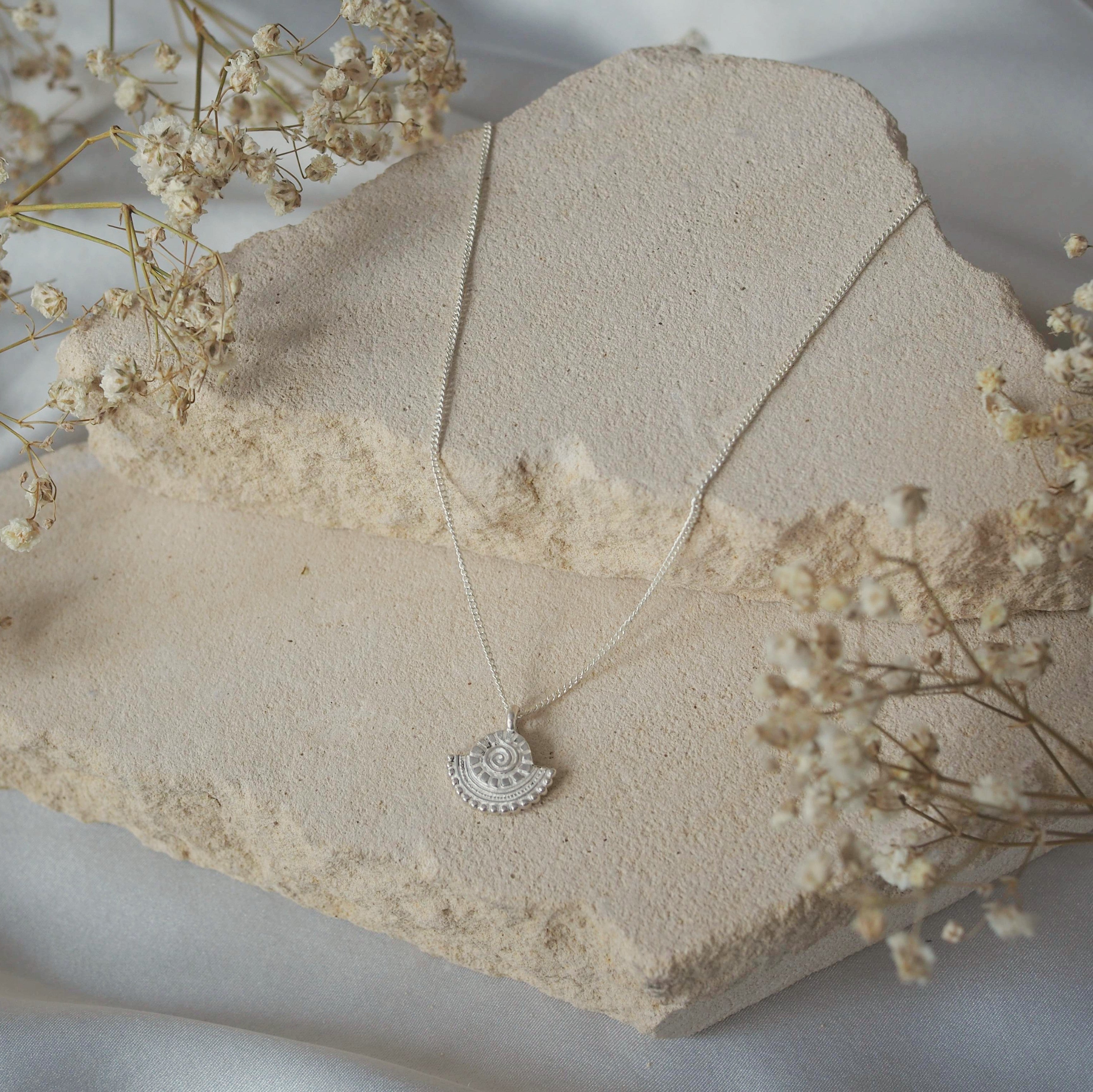 A jewelry display featuring a silver necklace arranged on beige stone pieces with dried flowers.