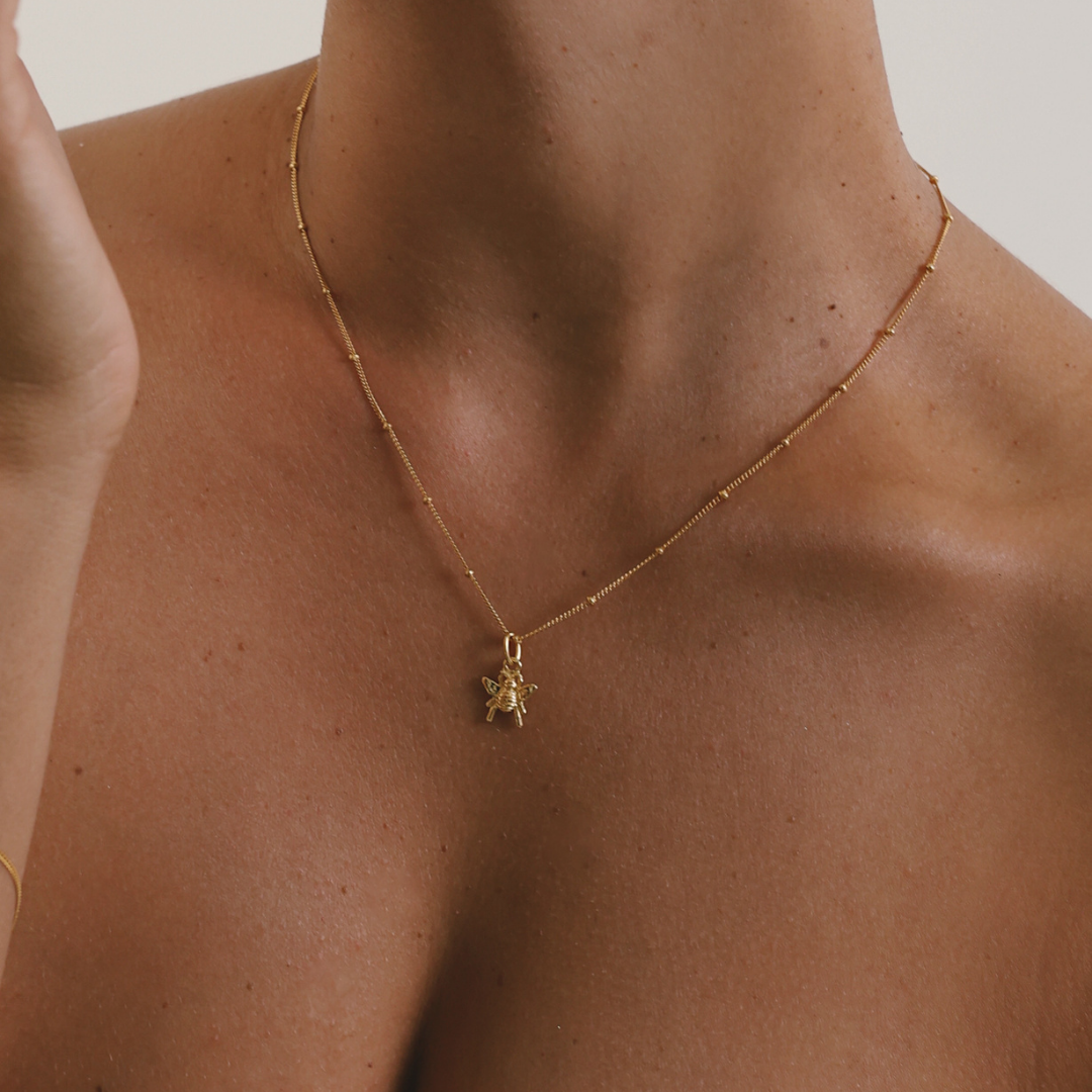 A delicate gold chain necklace with a small turtle pendant, shown worn on a model's neck and upper chest.