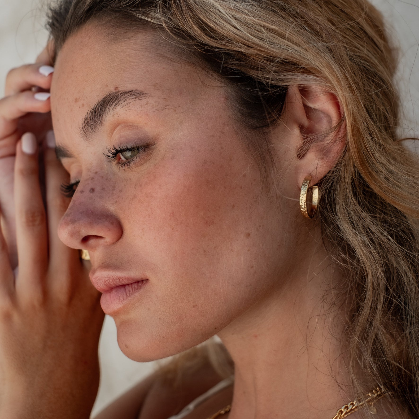 Close-up of a single hammered gold hoop earring worn on an ear with light brown hair.