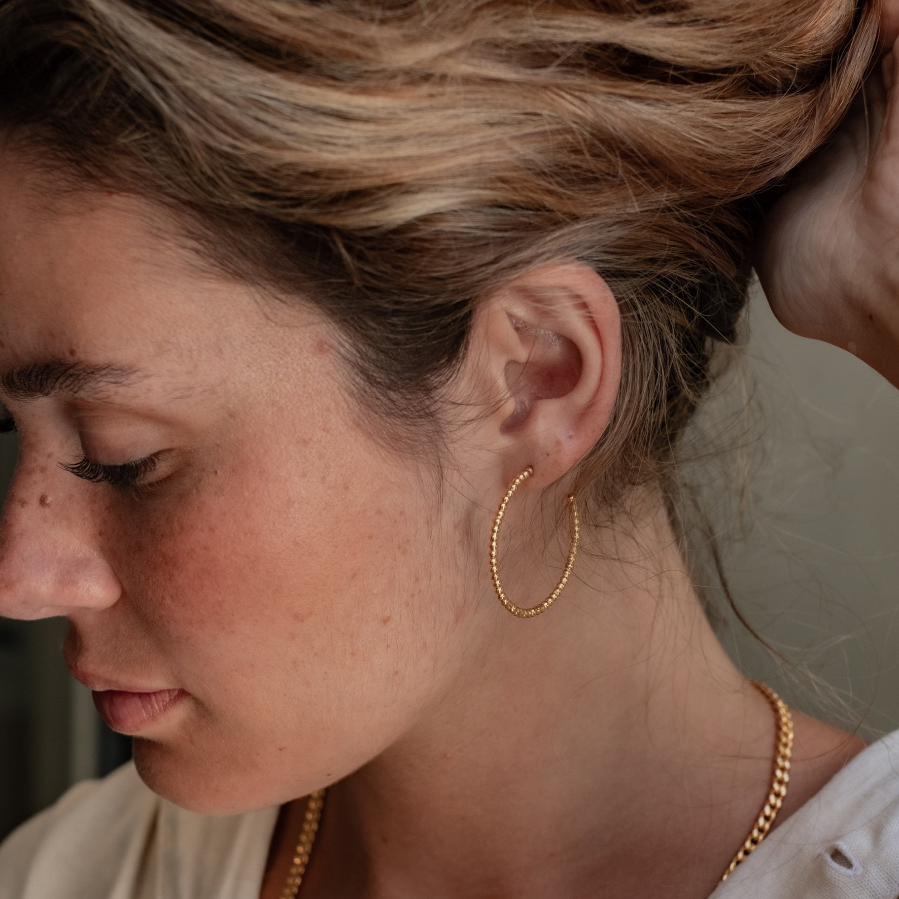 A woman with brown hair wearing a thin gold beaded earring