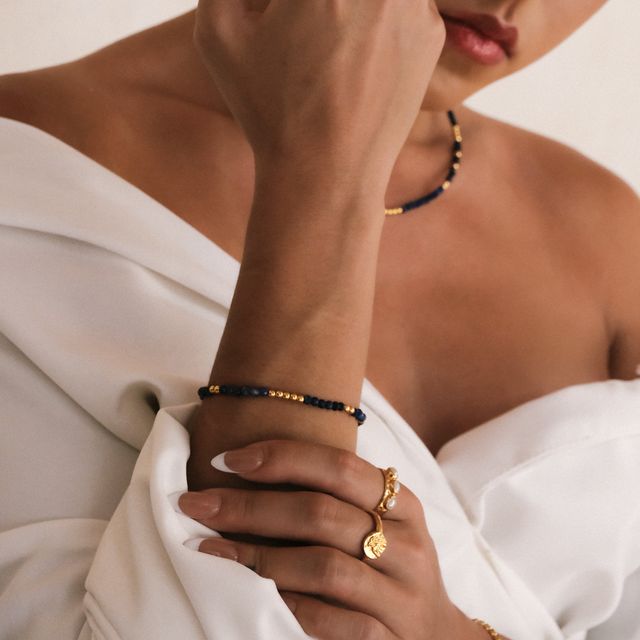 Glamorous woman accessorized with rings gold jewelry and blue color gemstone embellishment featuring on necklace and bracelet