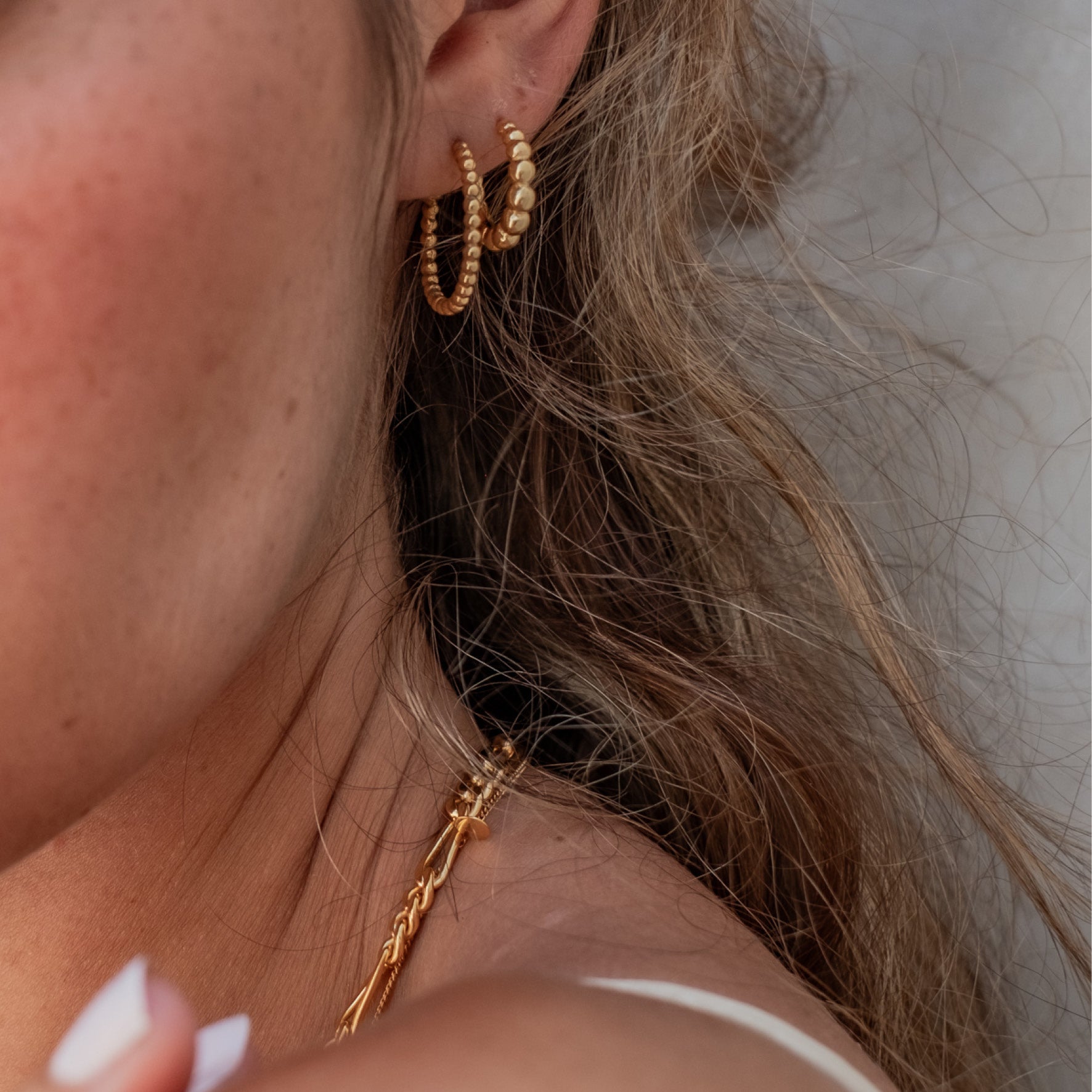 A woman with brown hair wearing thin gold beaded earrings