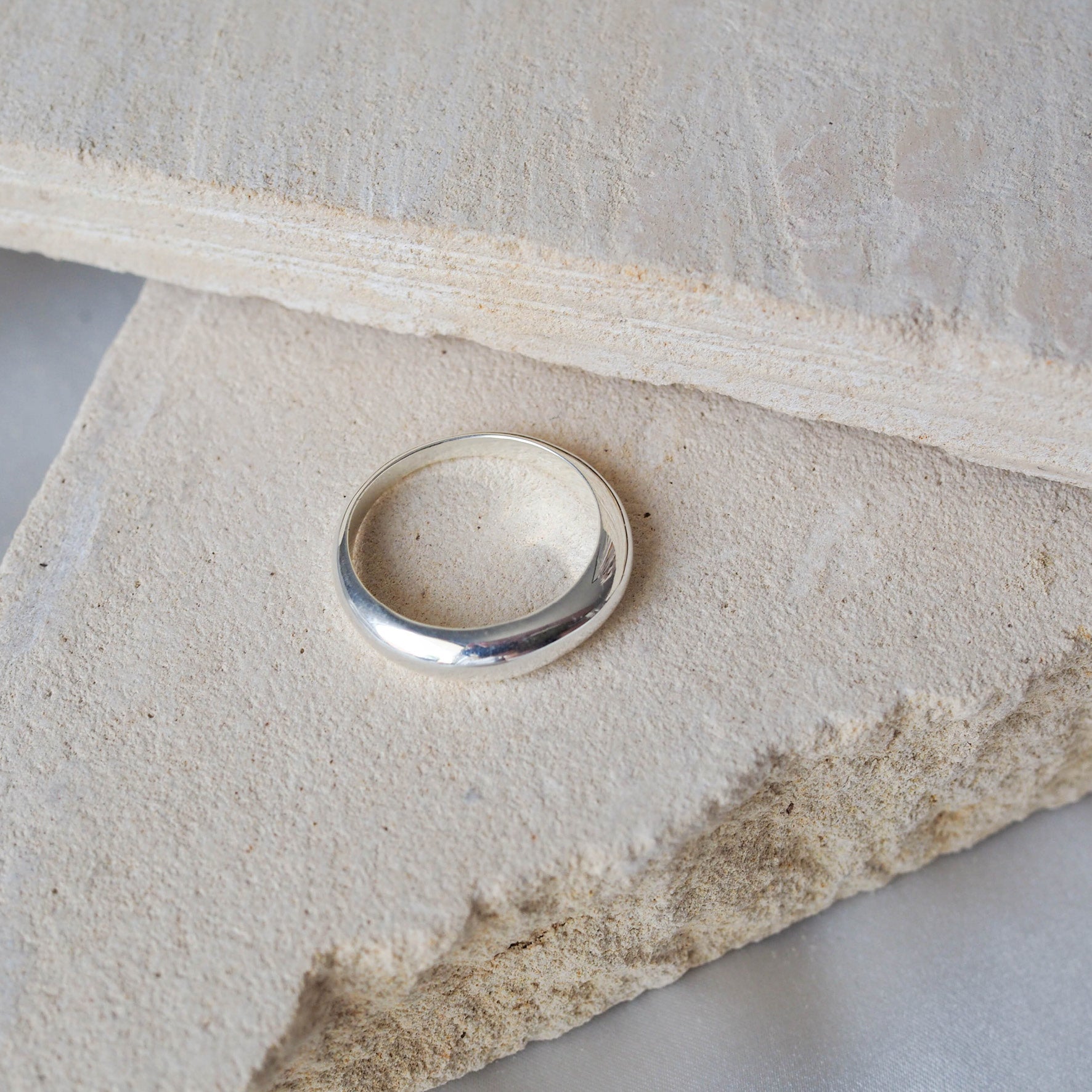 Close-up of a polished silver ring displayed on beige stone.
