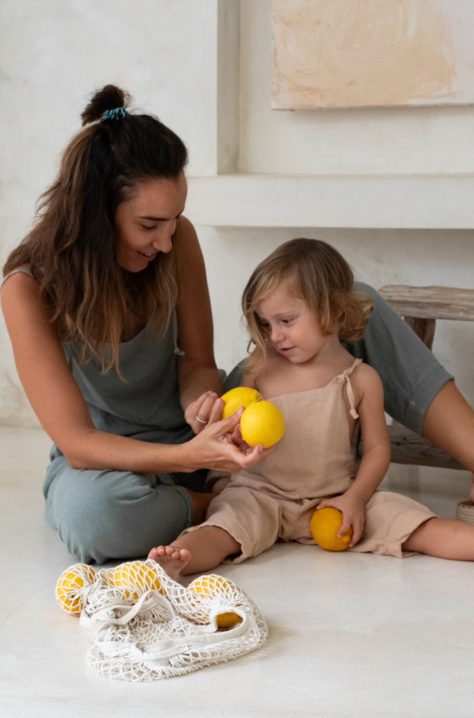 A toddler sitting together with a woman on the ground looking at some lemons