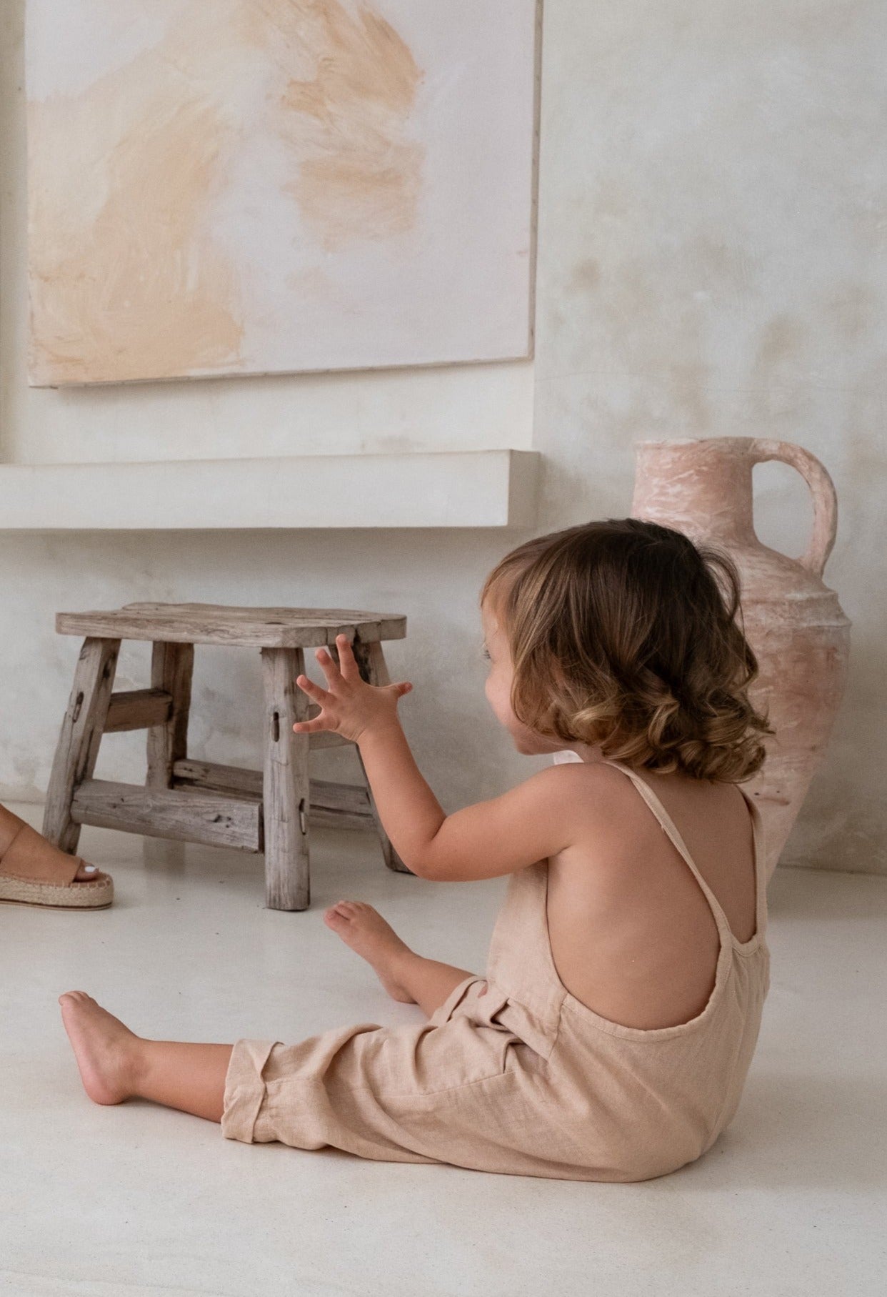 A toddler sitting on the ground wearing a brown overall