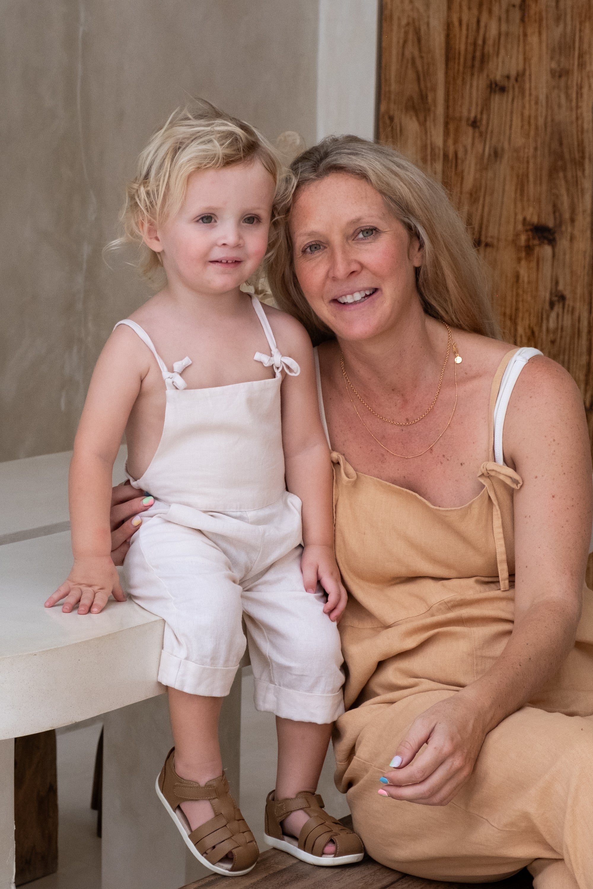 A child with blond hair wearing a white overall sitting next to a woman with a brown overall