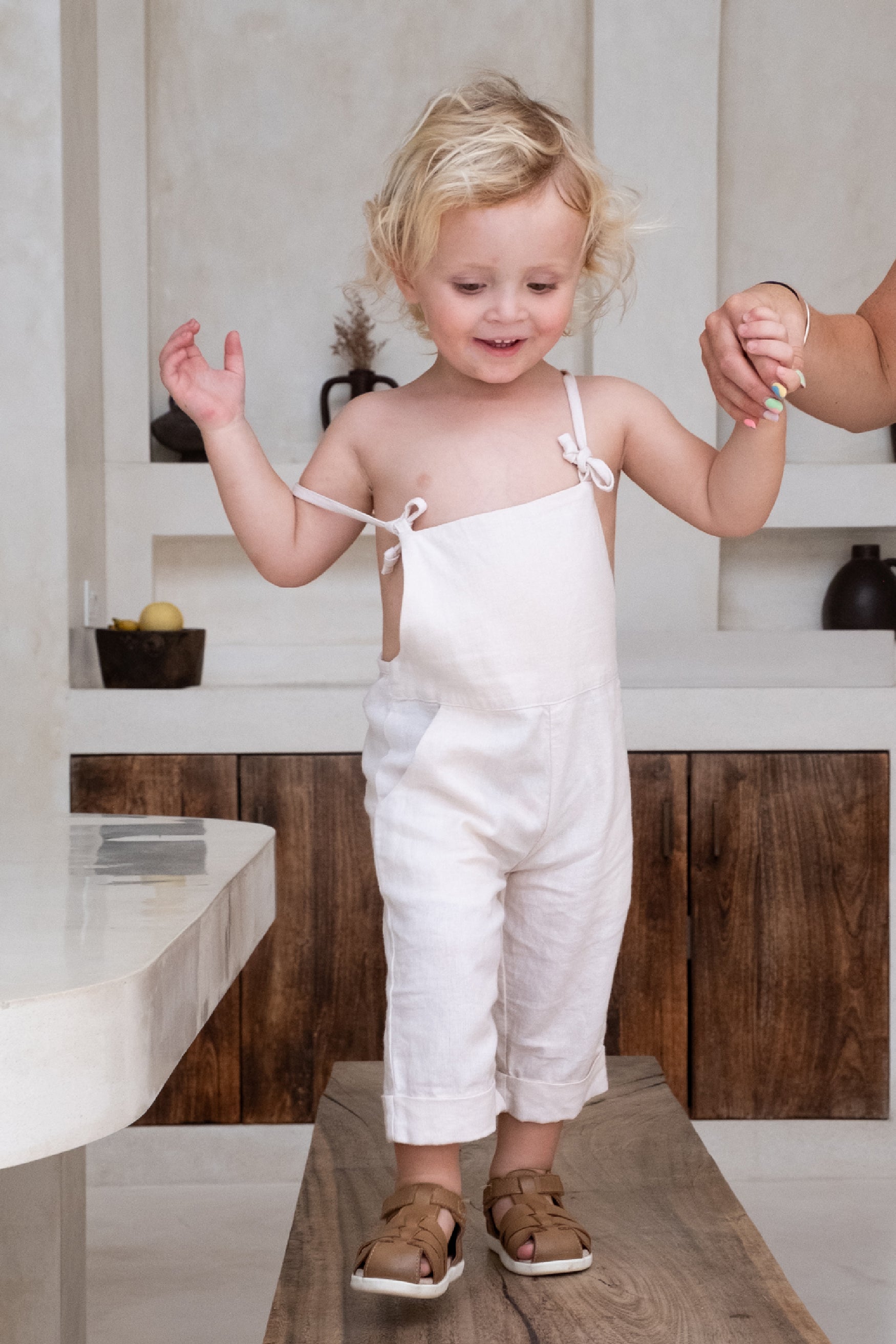 A child walkon on a wooden bench wearing a white overall