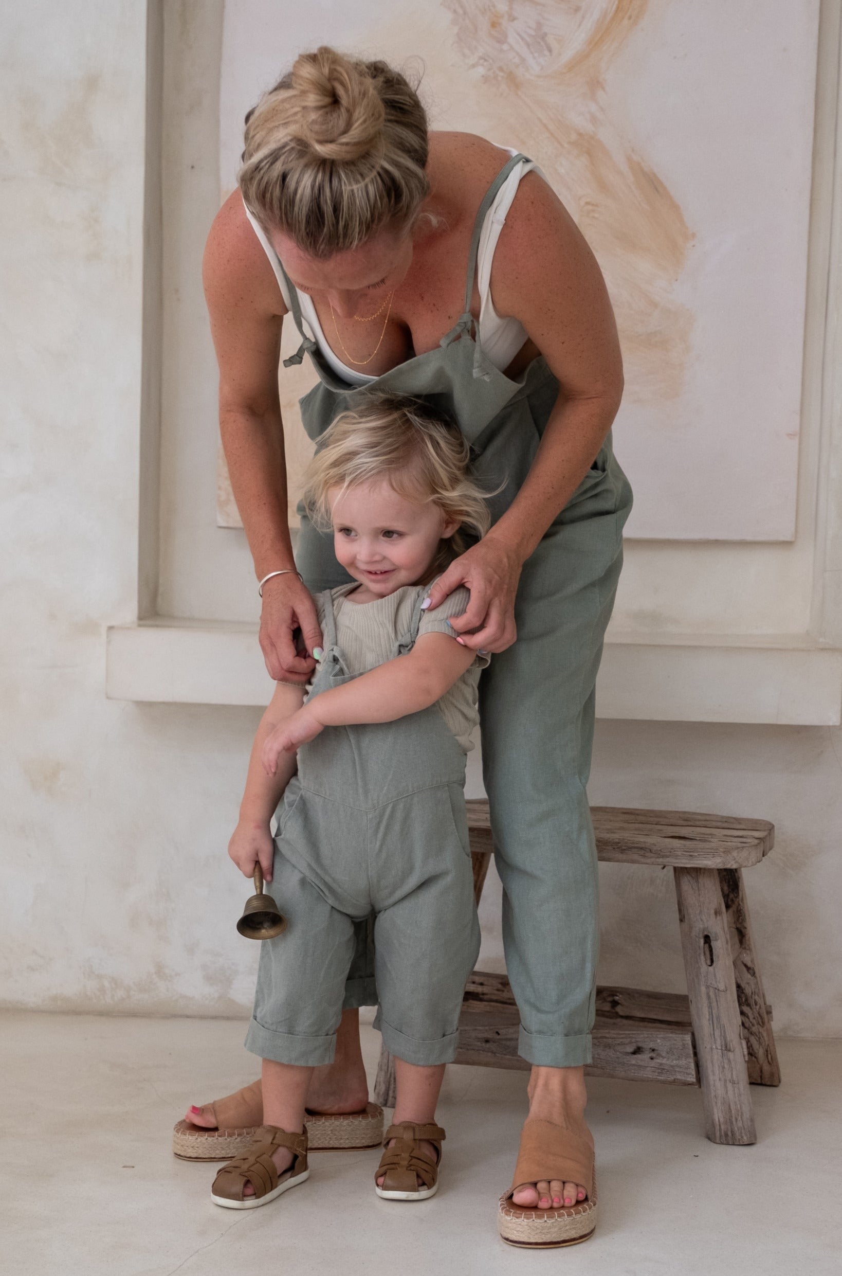 A toddler together with a woman both having blond hair and wearing an overall