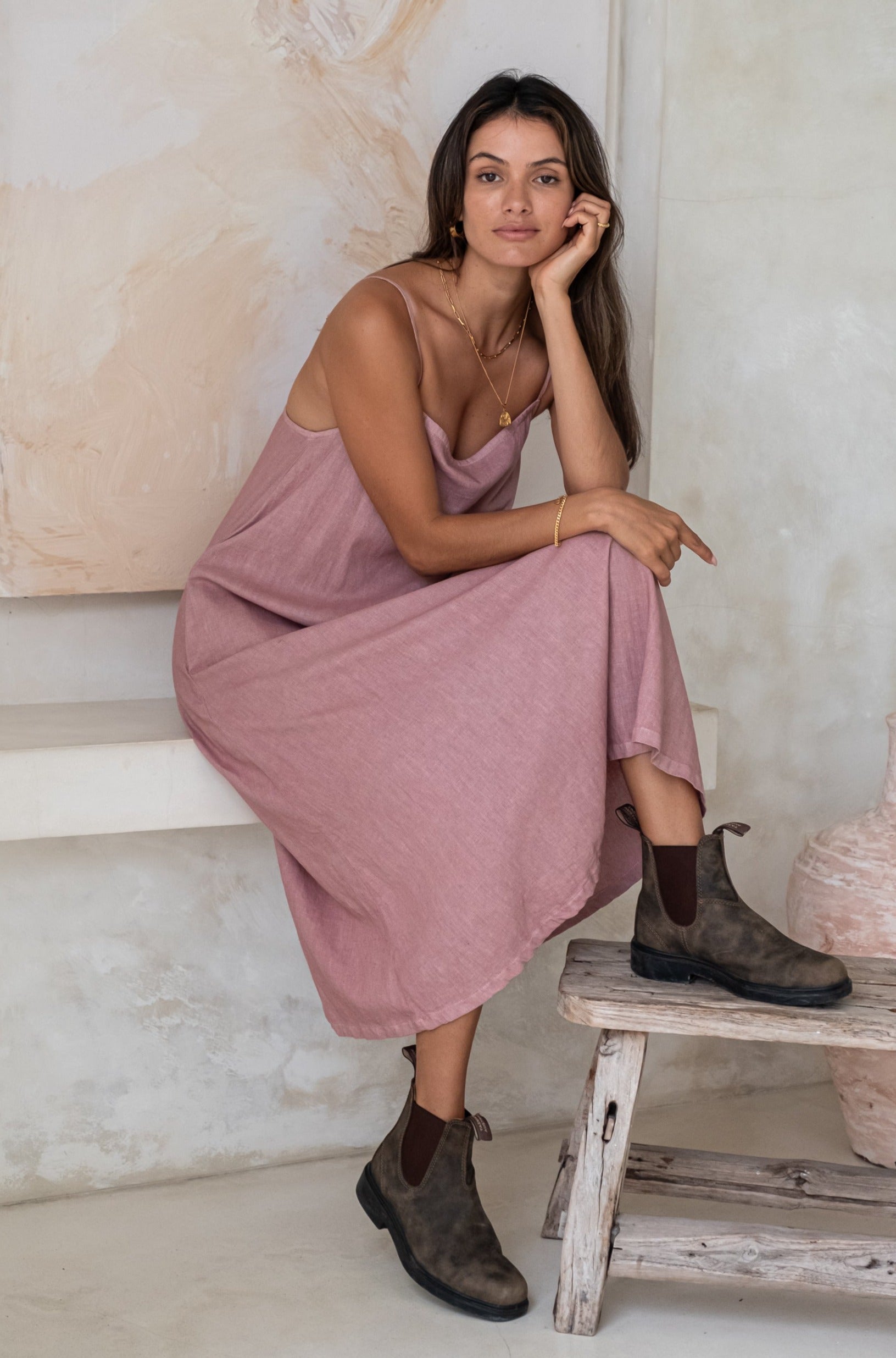 A woman wearing a pink midi dress and green boots while sitting in a minimalistic outdoor setting.