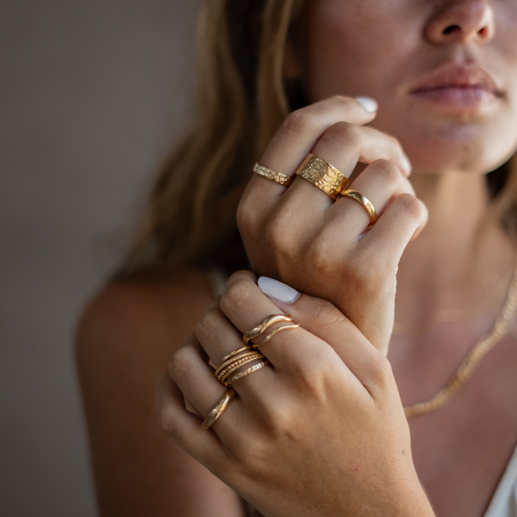 A person displaying an assortment of gold rings on both hands, highlighting various designs and textures.