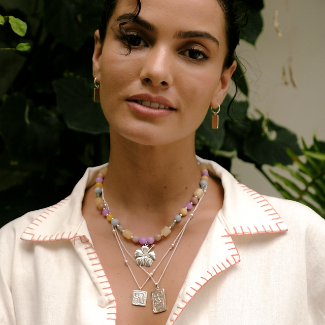 Woman wearing multiple necklaces with a white shirt against a green leafy background