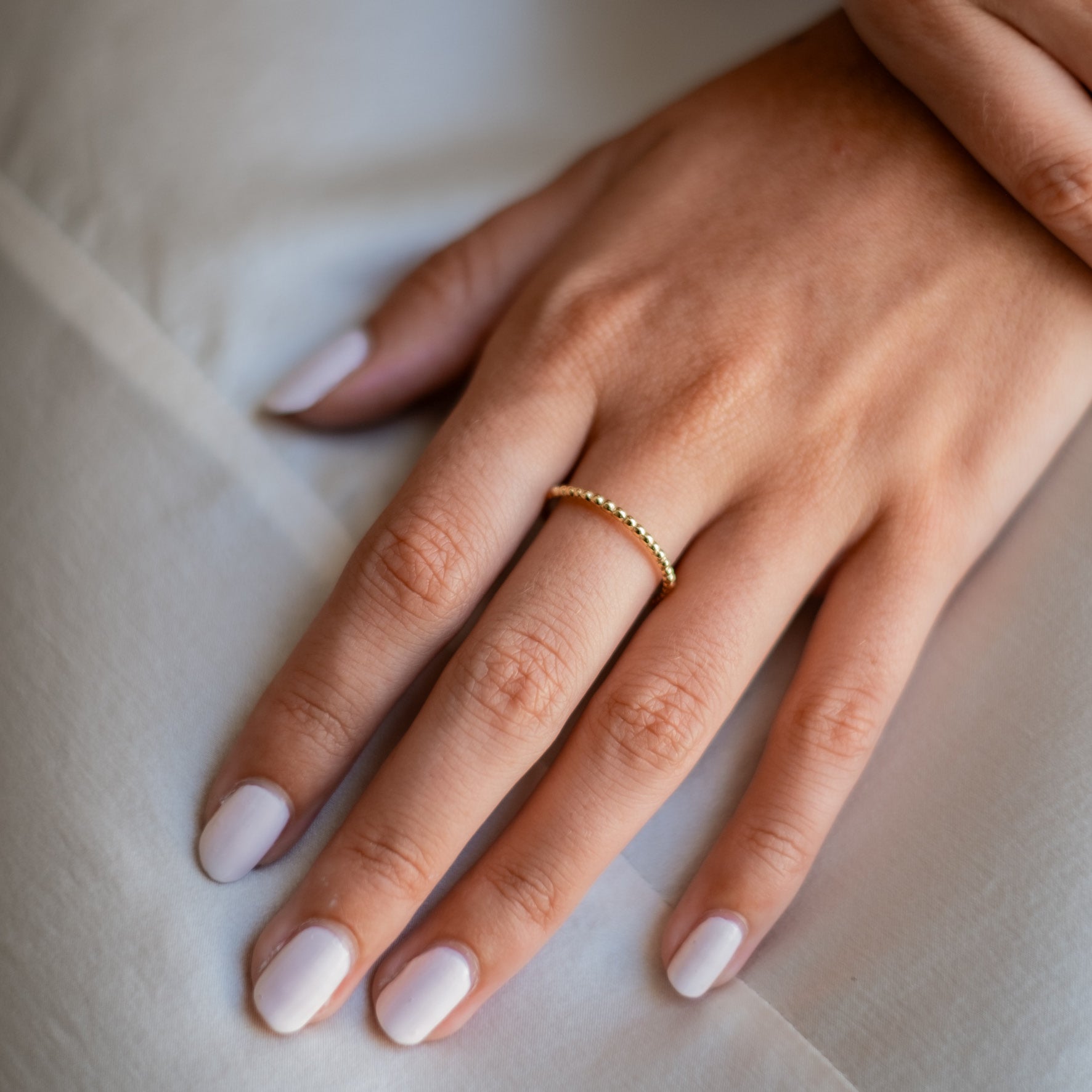 Close-up of a womans hand with white polished nails wearing a gold thin ring