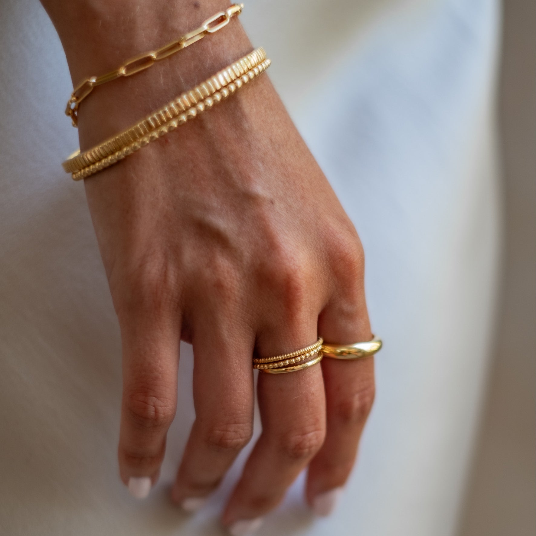 Close-up of a woman's hand wearing multiple gold jewellery on a white background