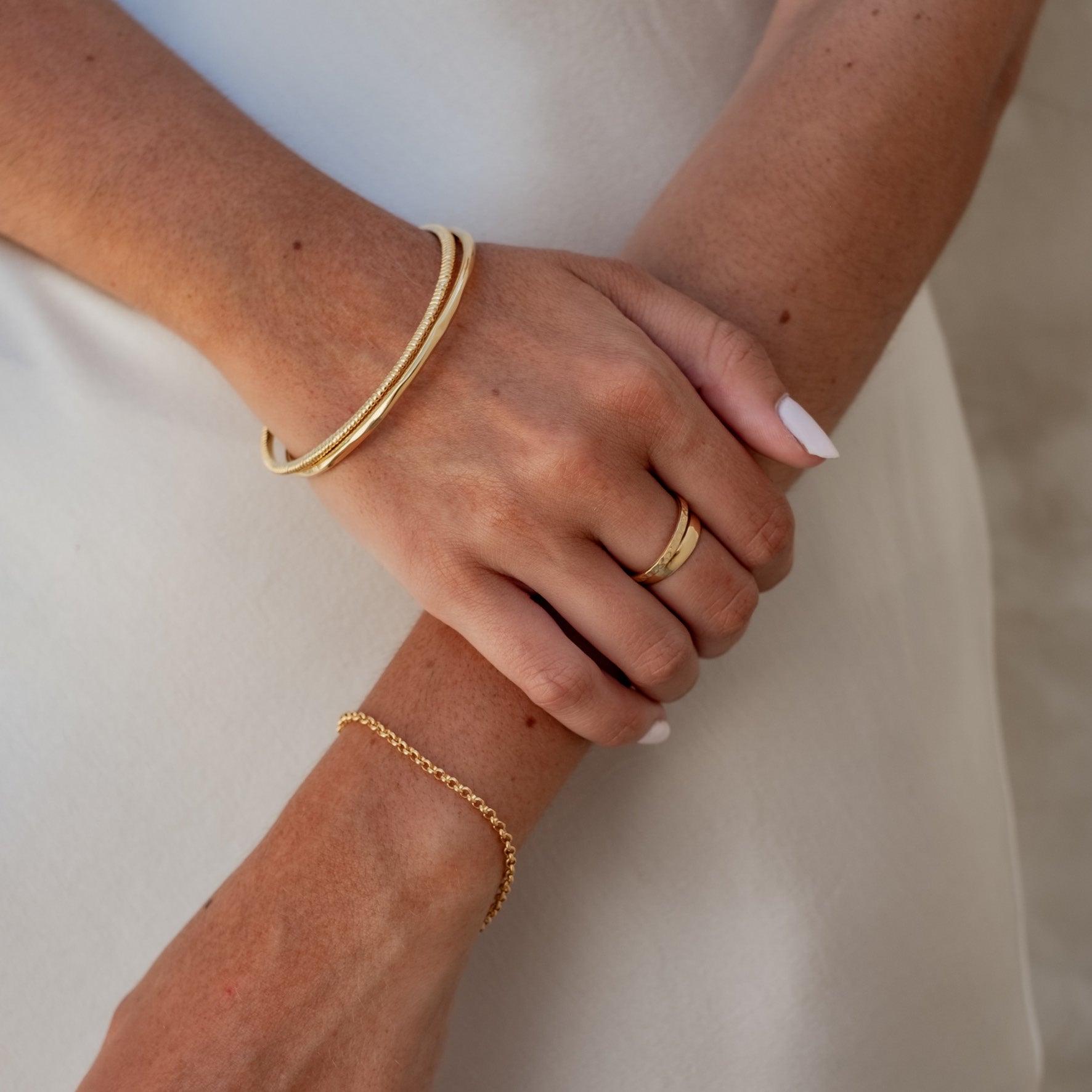 A woman covering her eyes with one hand, wearing multiple silver rings and white nail polish.