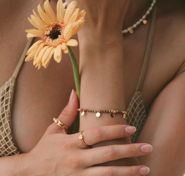 Woman gently holding a flower, highlighting her gold bracelet and polished gold ring