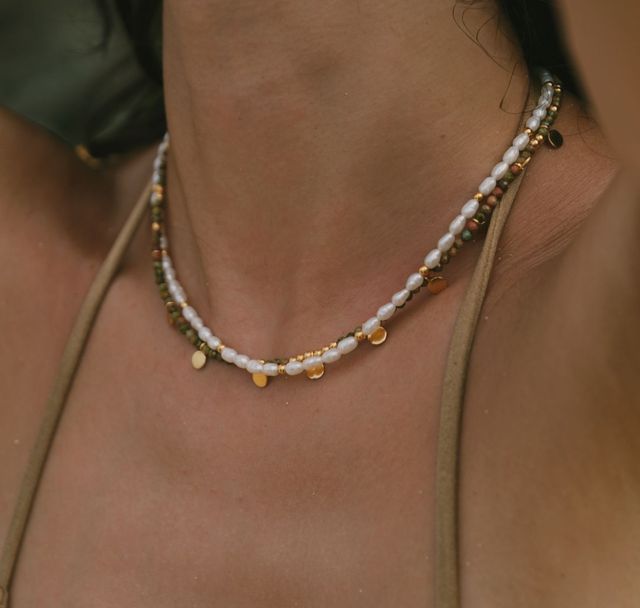 Close-up of layered jewelry featuring a pearl necklace and sienna necklace