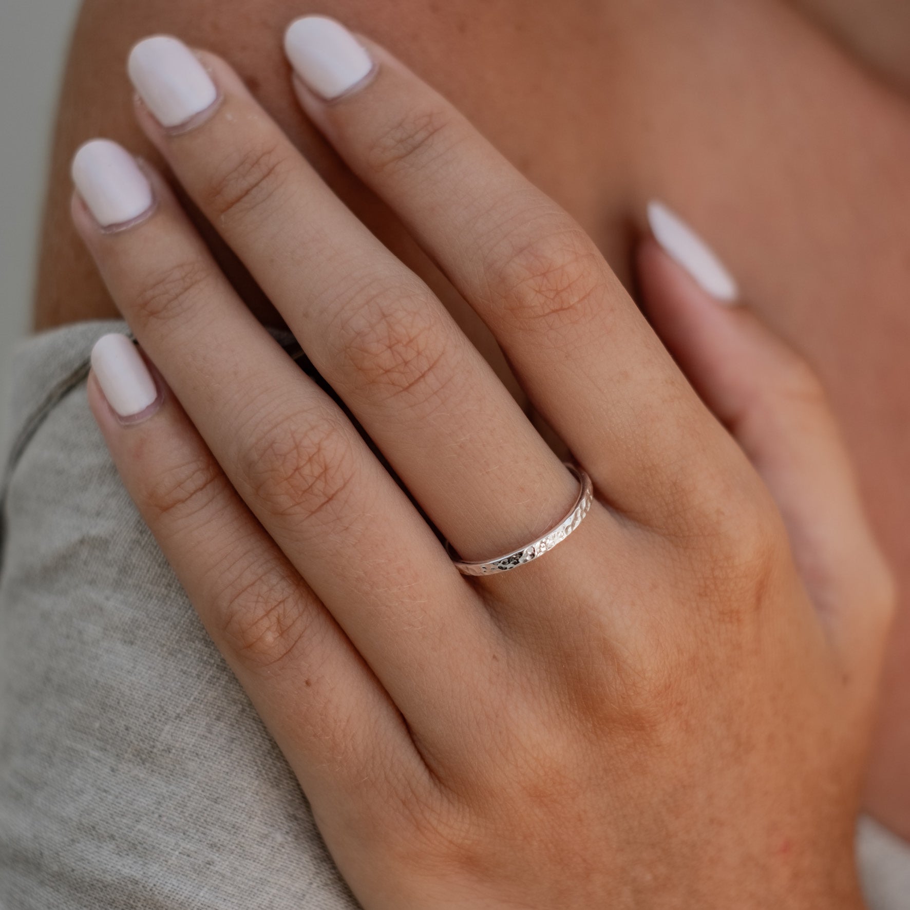 A close-up of a hand wearing a wide silver hammered ring.