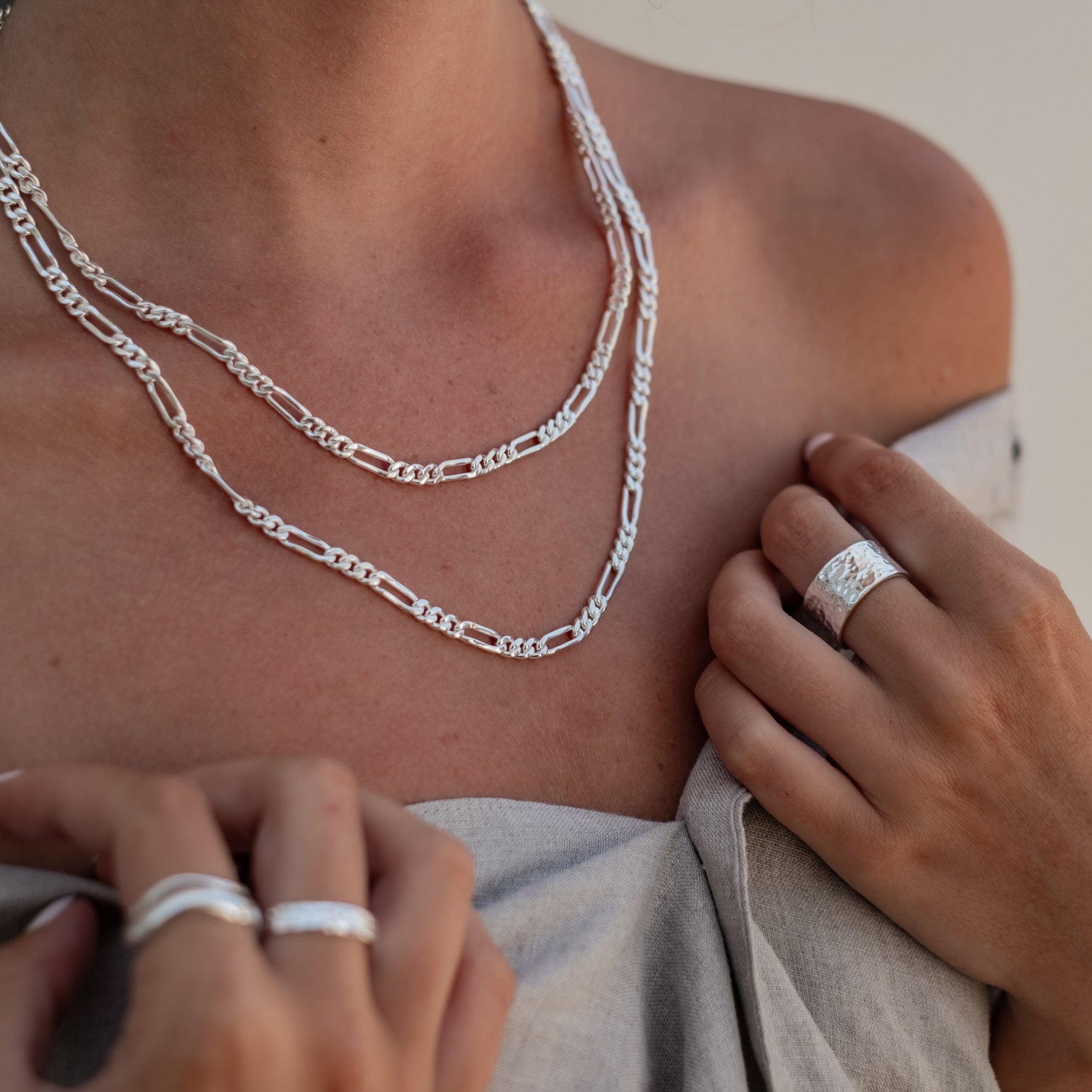 A woman wearing layered silver chain necklaces and multiple silver rings on her fingers.