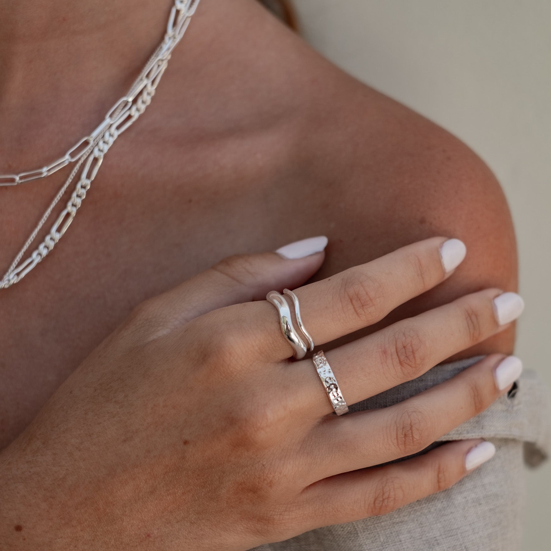 A close-up of a hand wearing a wide silver hammered ring.