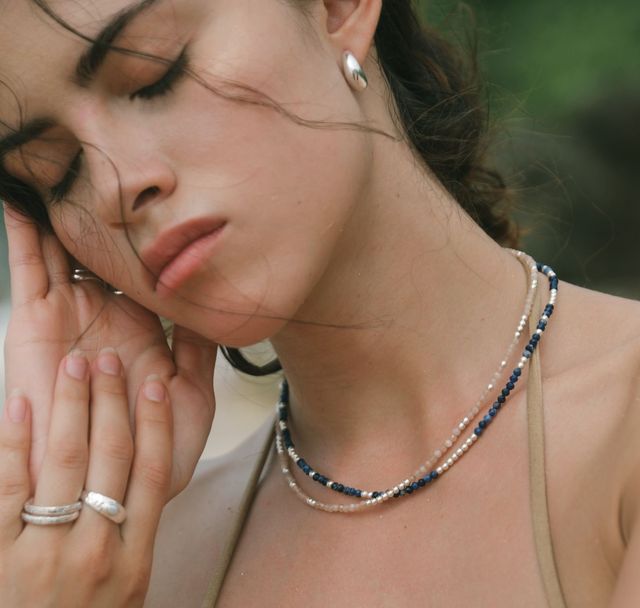 a woman who is closing her eyes wearing multiple silver necklaces and multiple silver rings