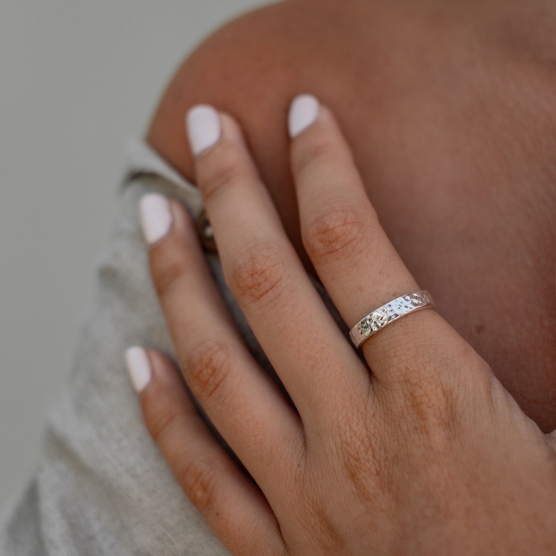 A close-up of a hand wearing a wide silver hammered ring.