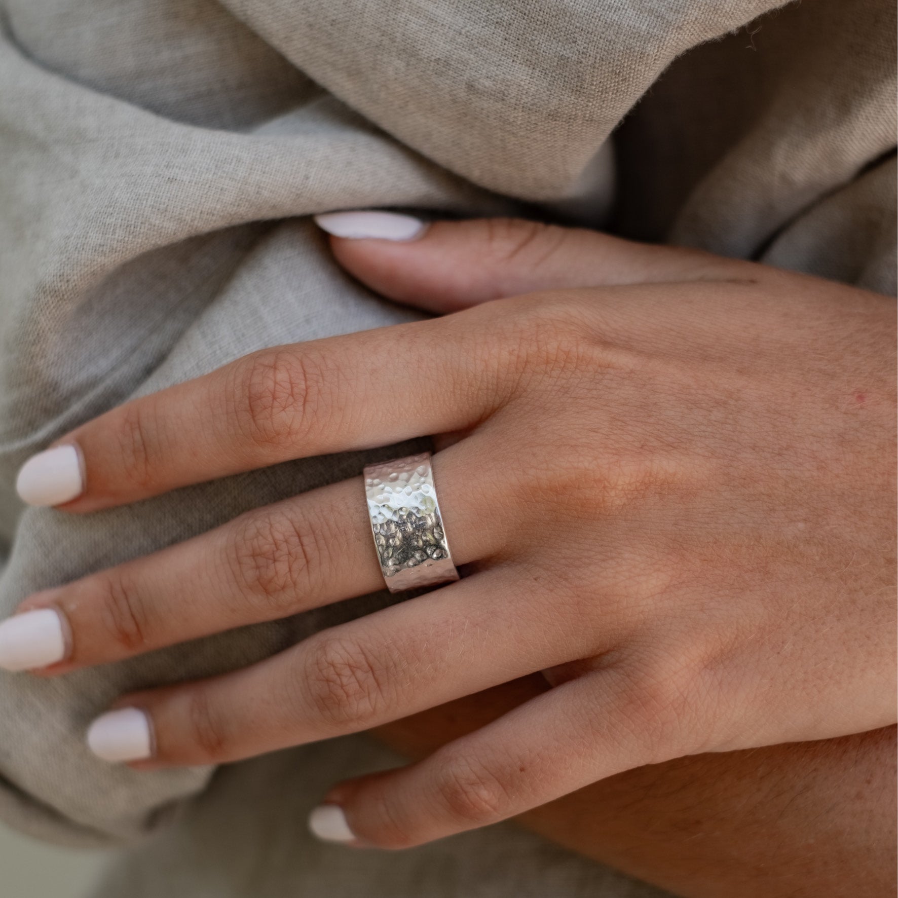 A close-up of a hand wearing a wide silver hammered ring.