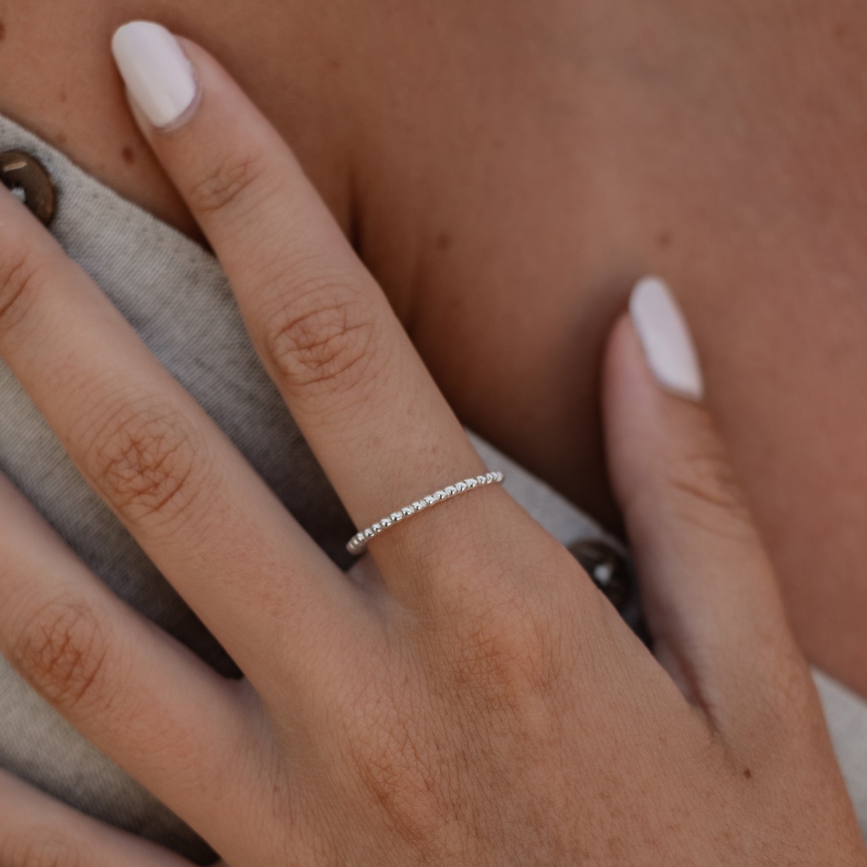 Close-up of a womans hand with white polished nails wearing a silver thin ring