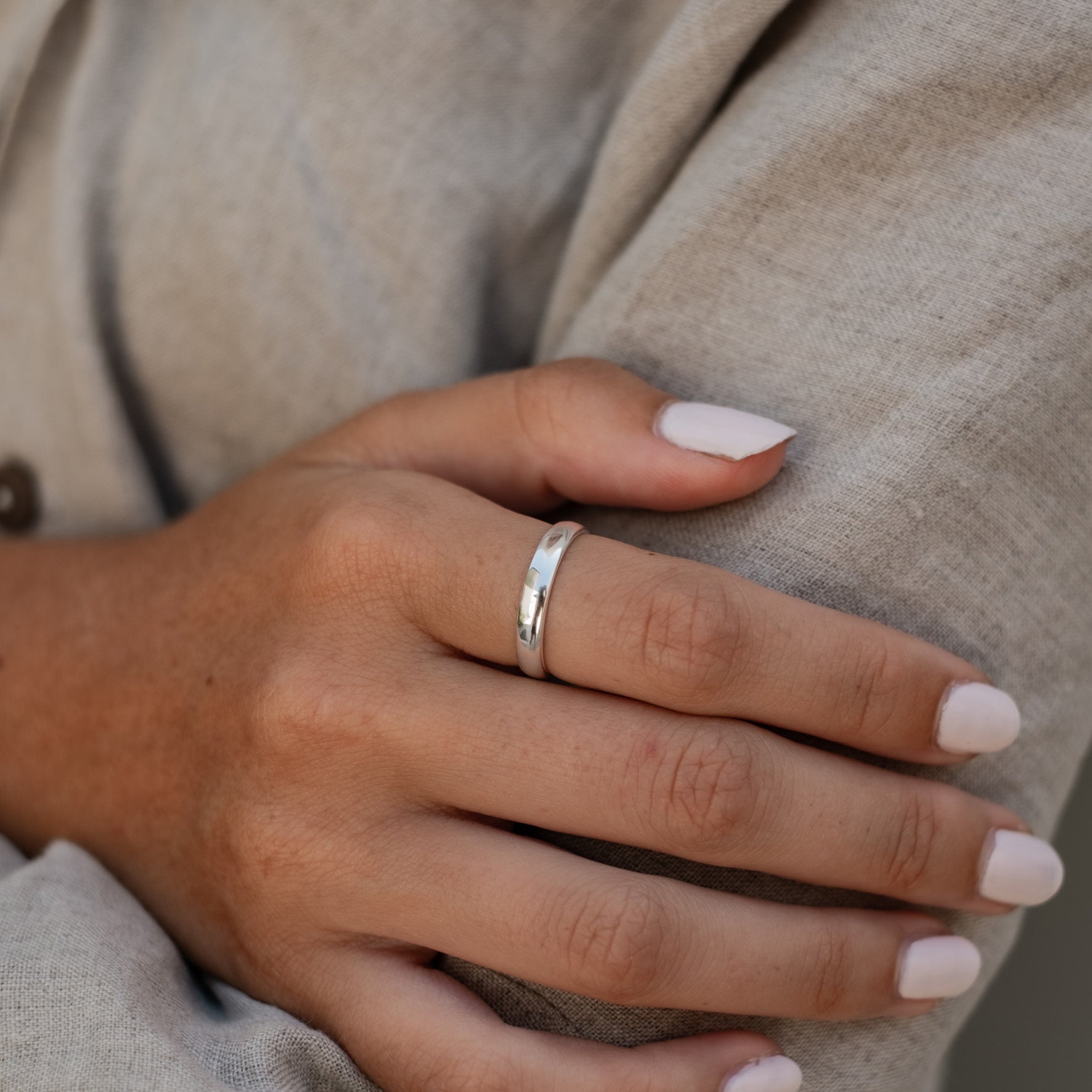 A person wearing a simple silver ring, with their arms crossed and sporting white manicured nails.